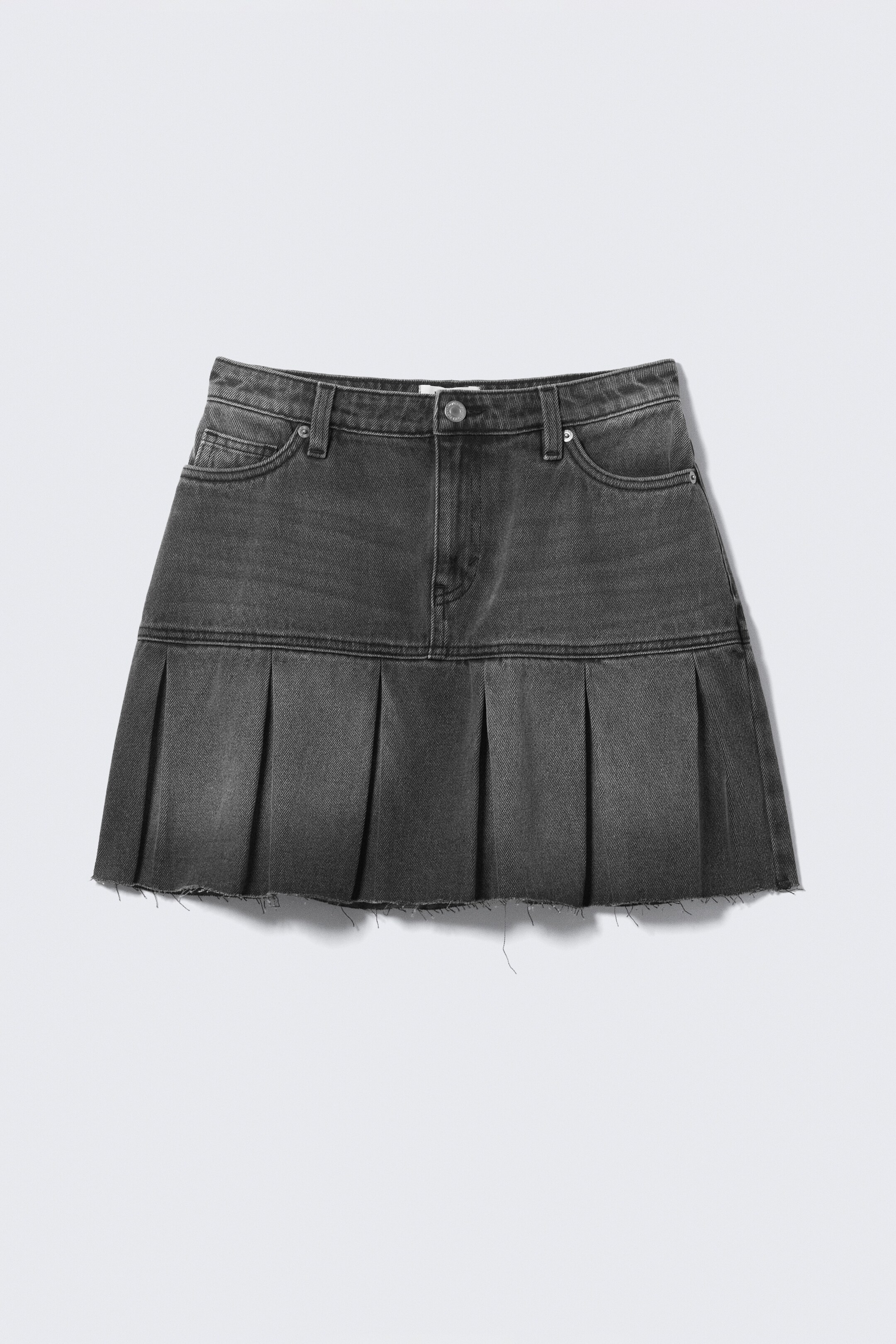 Visualizza immagine più grande: Una minigonna a vita bassa è visibile dalla parte anteriore, realizzata in twill di cotone grigio scuro e caratterizzata da un classico design a cinque tasche con chiusura a zip e bottone. Le pieghe a scatola ben pressate formano la sua silhouette strutturata e svasata, rifinita con un bordo grezzo.