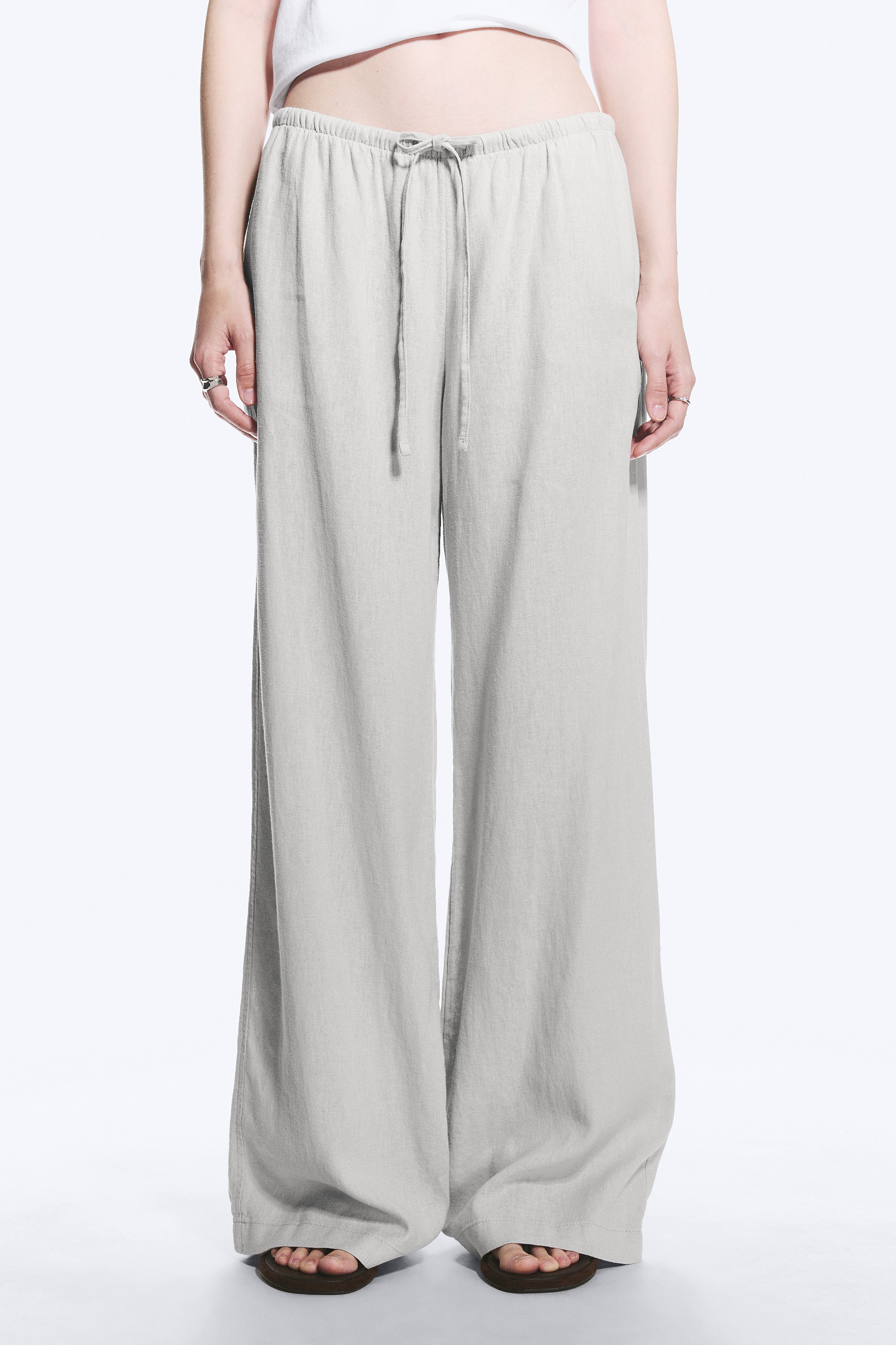 Agrandir l'image: Pantalon large gris clair avec taille élastiquée à cordon de serrage et coupe décontractée, l'ourlet pleine longueur se posant élégamment sur les chaussures du porteur.