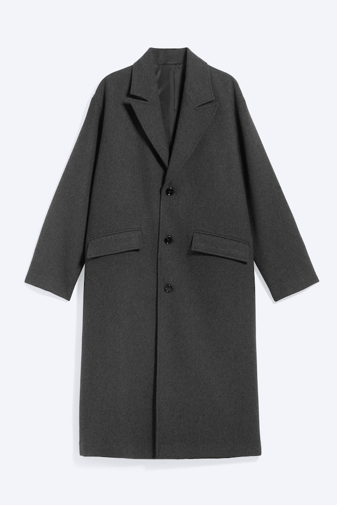 Um casaco cinzento-escuro de abotoamento simples é apresentado de frente, evidenciando uma silhueta oversized com lapelas de entalhe e um fecho frontal de três botões. Apresenta dois bolsos frontais com pala e mangas longas e estruturadas. - 1