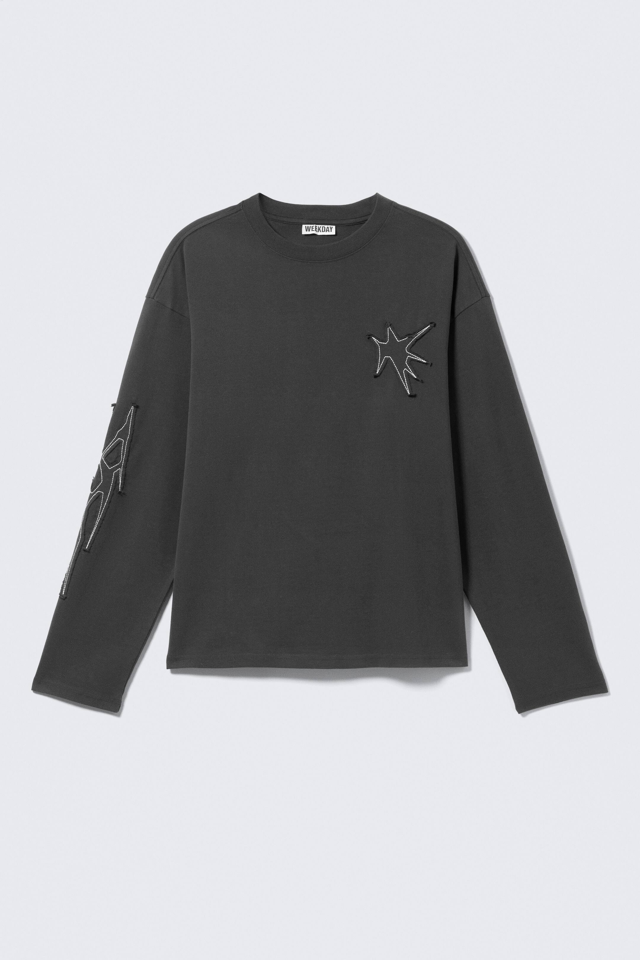 Größeres Bild ansehen: Ein dunkelgraues Langarm-T-Shirt wird als FRONT präsentiert, mit einem gerippten Rundhalsausschnitt und einer entspannten, kastigen Passform. Es zeigt eine unregelmäßige, sternenähnliche Umrissform auf der linken Brust und abstrakte Ausschnittdesigns entlang des linken Ärmels, beide erstellt mit weißer Kordel und kleinen schwarzen Befestigungen.