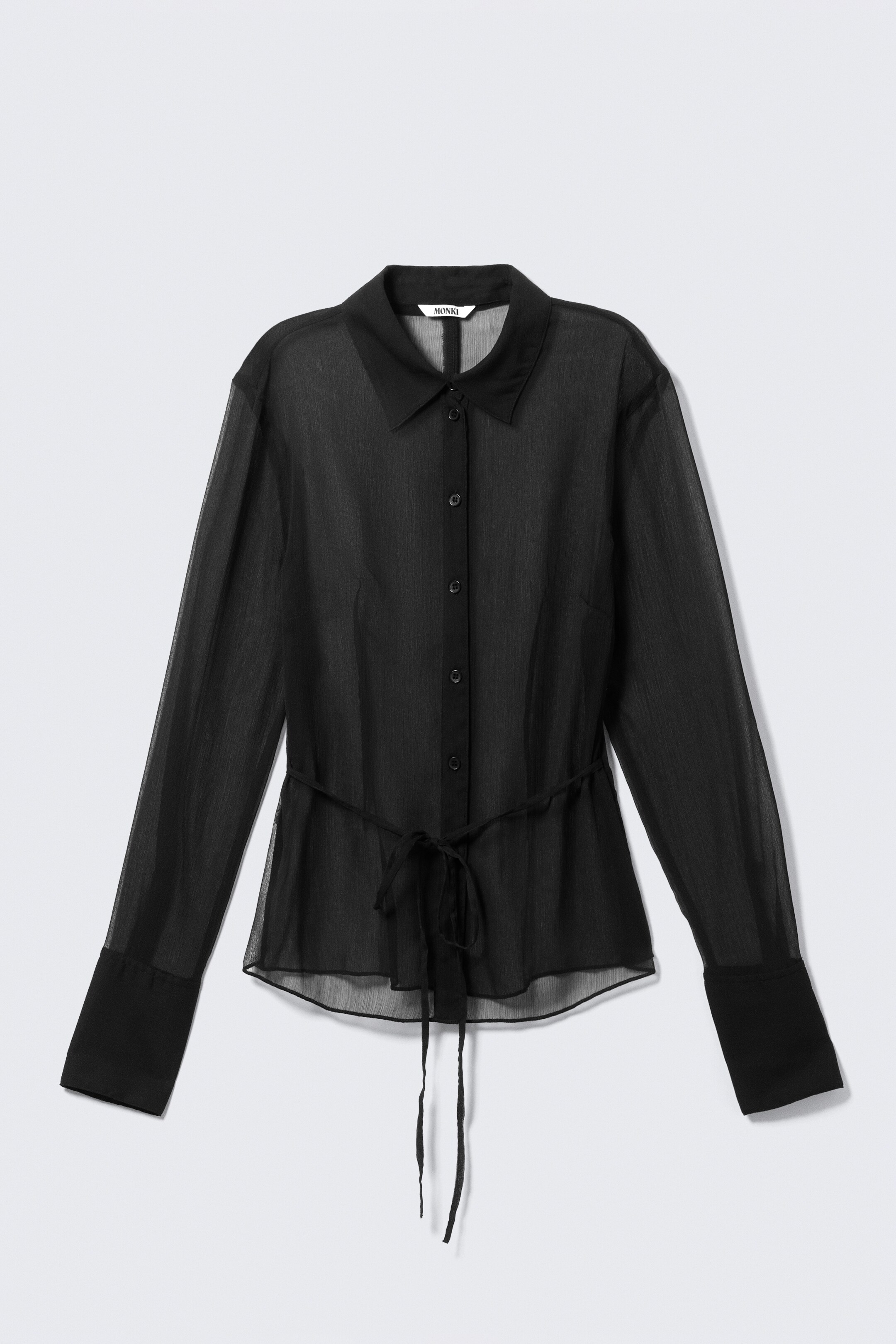 Ingrandisci l'immagine: Una camicia nera trasparente a maniche lunghe è presentata dal DAVANTI, caratterizzata da un colletto a punta, un listino frontale con bottoni e maniche lunghe con polsini svasati. Le pince sul davanti modellano il busto, mentre i dettagli regolabili a cravatta sul retro stringono la vita, annodati sul davanti, con un orlo curvo che completa il design.