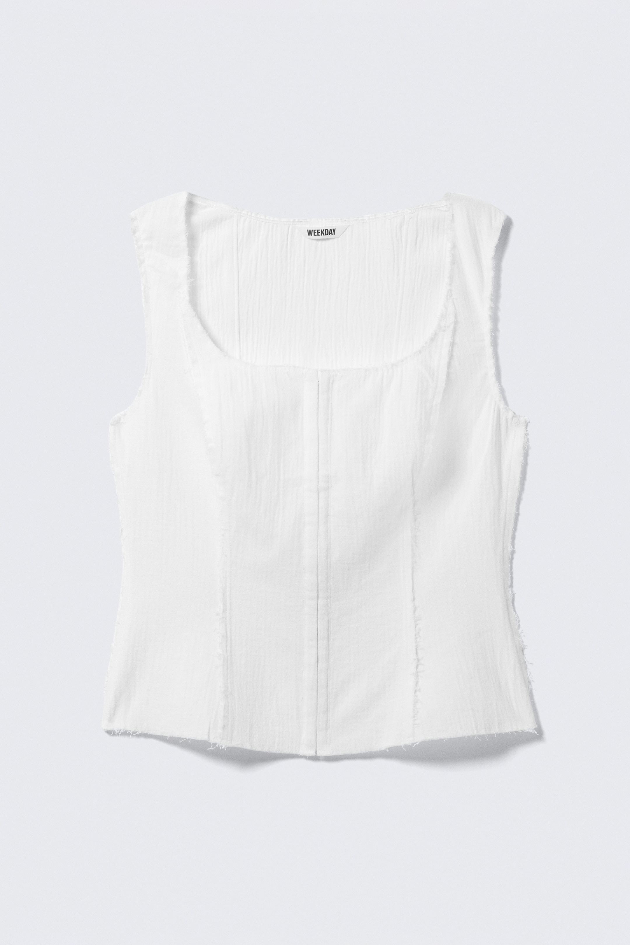 Ver imagem maior: Um top branco, voltado para a FRENTE, estilo espartilho, apresenta um decote quadrado e bordas cortadas ao natural ao longo do decote, cavas e bainha. É confeccionado em sarja de algodão texturizada, exibindo costuras de painéis estruturadas com detalhes visíveis de pesponto, e um fecho frontal completo de gancho e olho ao longo do centro.
