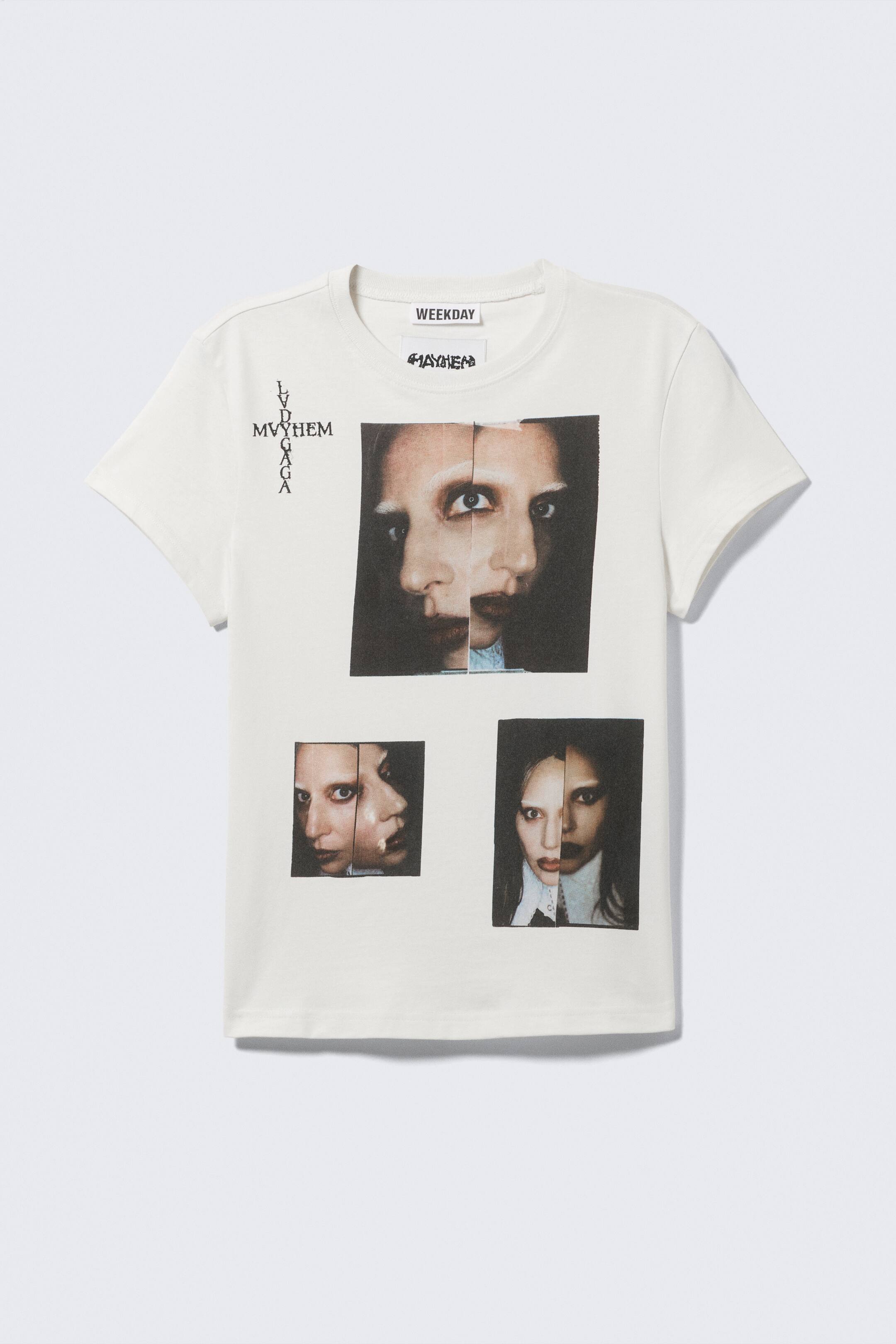 Agrandir l'image: Un t-shirt crème à manches courtes présente son devant, affichant de manière proéminente un grand imprimé graphique d'un visage fendu, avec deux images faciales plus petites positionnées en dessous. Un texte vertical lisant "LVD MVYHEM GAGA" est disposé sur le côté gauche, tandis que le mot "MAYHEM" est visible sur une étiquette près de l'encolure ronde.