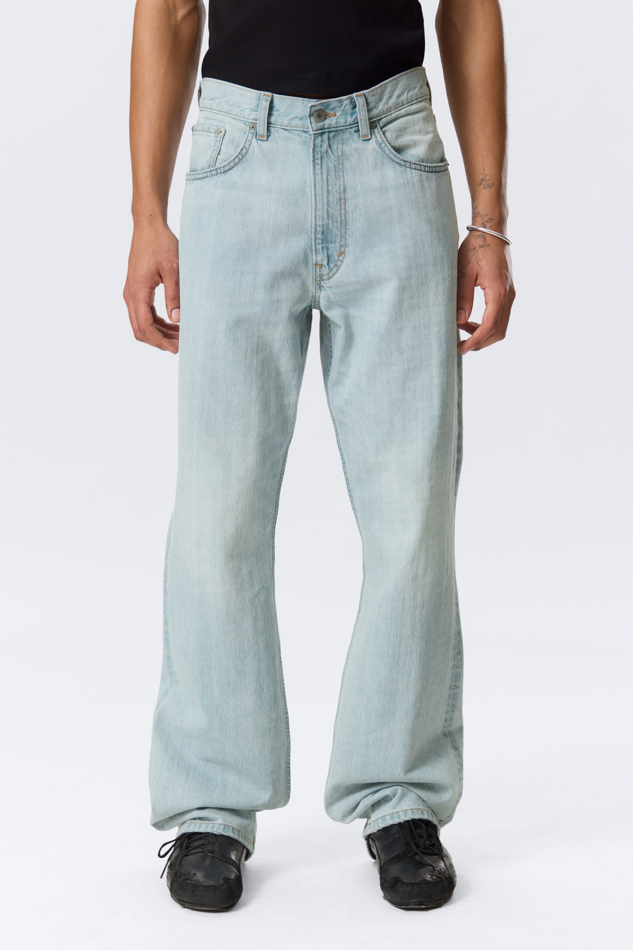 Visualizza immagine più grande: I jeans azzurri presentano un lavaggio sbiadito, una vestibilità rilassata e un design a gamba larga, mostrati da una vista frontale a lunghezza intera. I jeans mostrano una chiusura con bottone e cerniera in vita, tasche frontali curve e un piccolo taschino per le monete, con le gambe larghe che si appoggiano leggermente sopra scarpe nere.