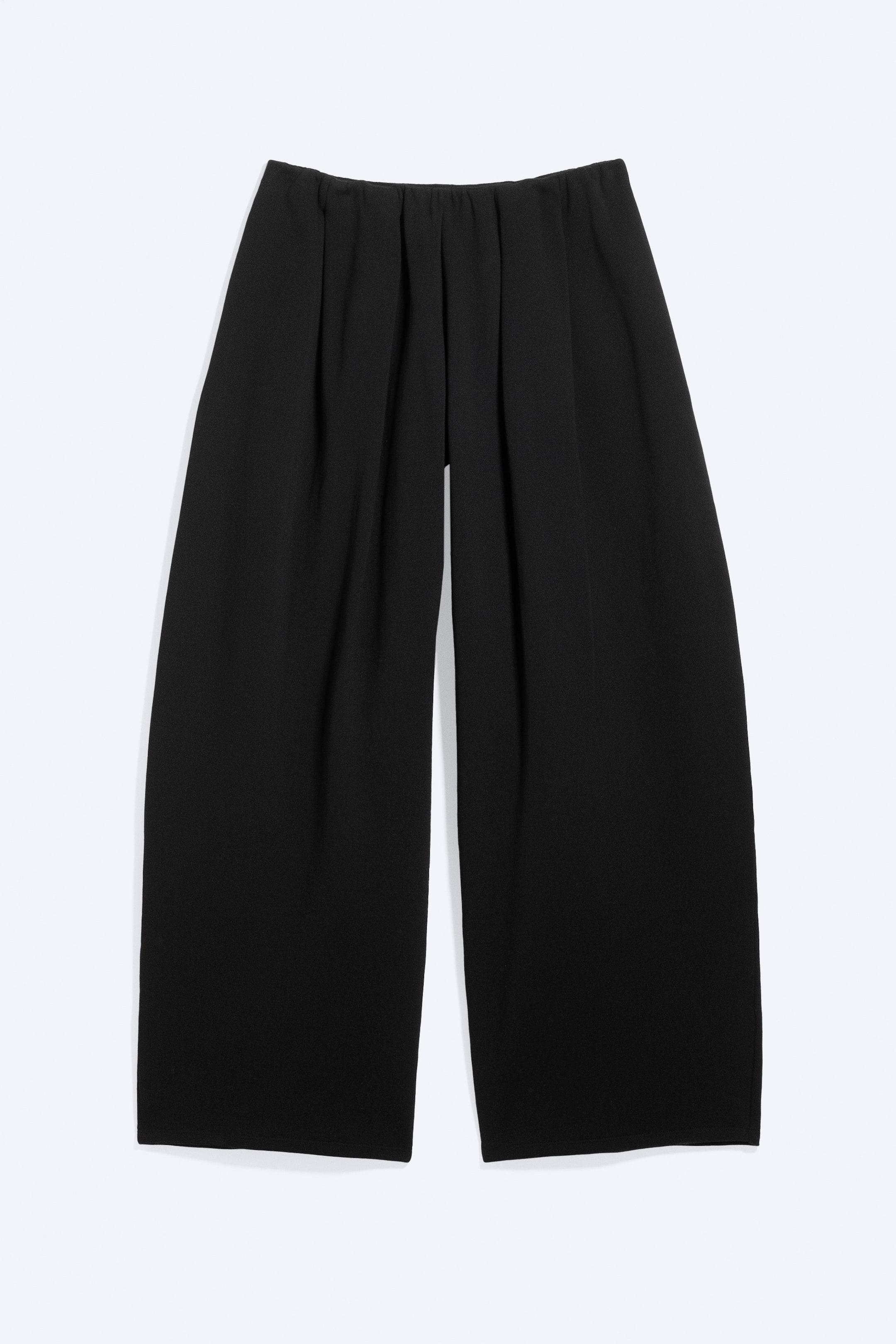Ver imagen más grande: Pantalones culotte negros vistos desde el frente, con una cintura elástica fruncida. El diseño incluye pliegues verticales que se originan en la cintura y se extienden hacia unas piernas anchas y fluidas.