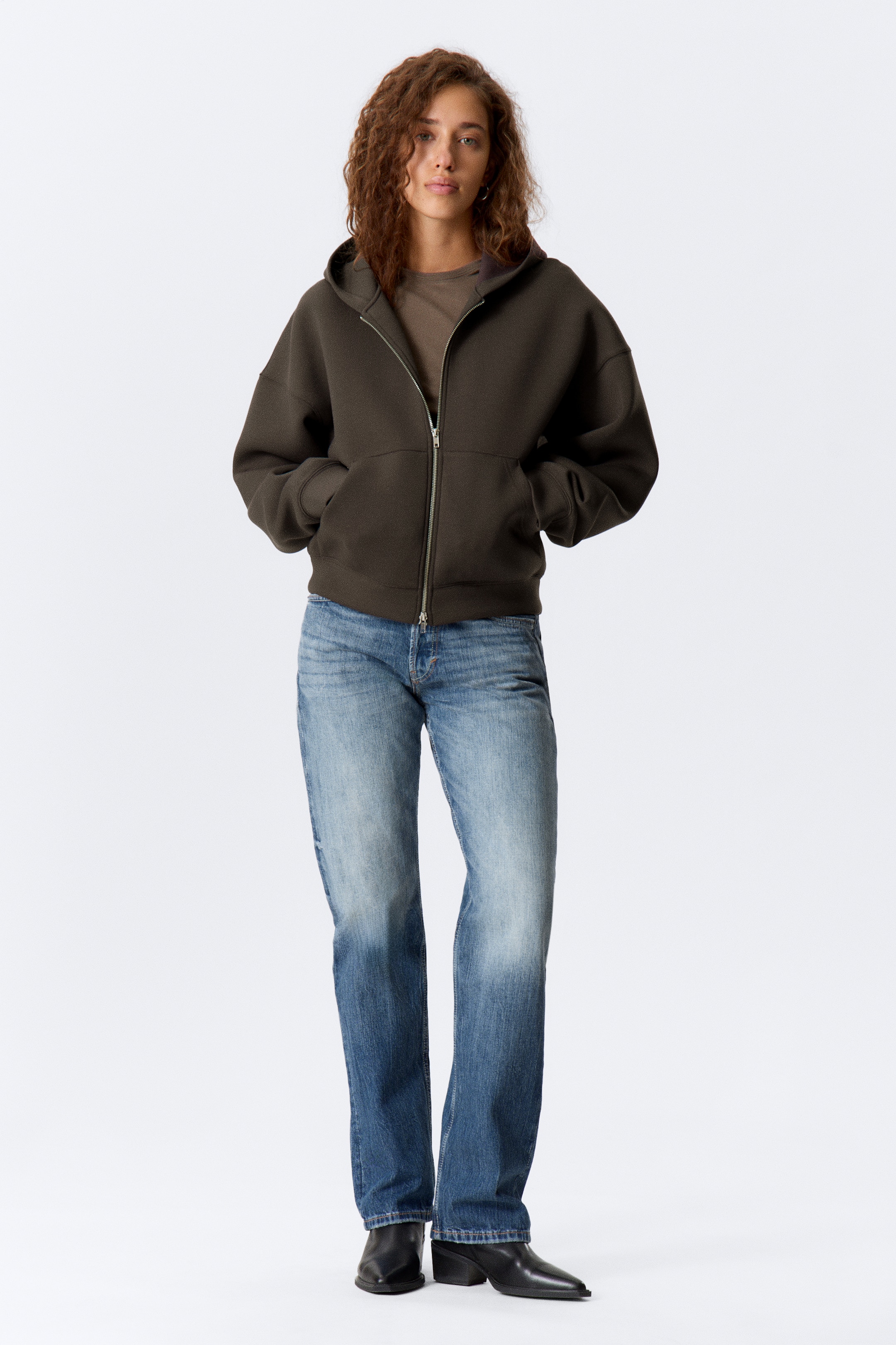 Agrandir l'image: Un sweat à capuche zippé marron foncé est orienté vers l'avant, avec une fermeture éclair argentée sur toute la longueur et des poches kangourou à l'avant. Il présente une coupe décontractée avec des poignets et un ourlet côtelés, ainsi qu'une capuche avec un cordon de serrage, tandis qu'un t-shirt marron clair est superposé en dessous.