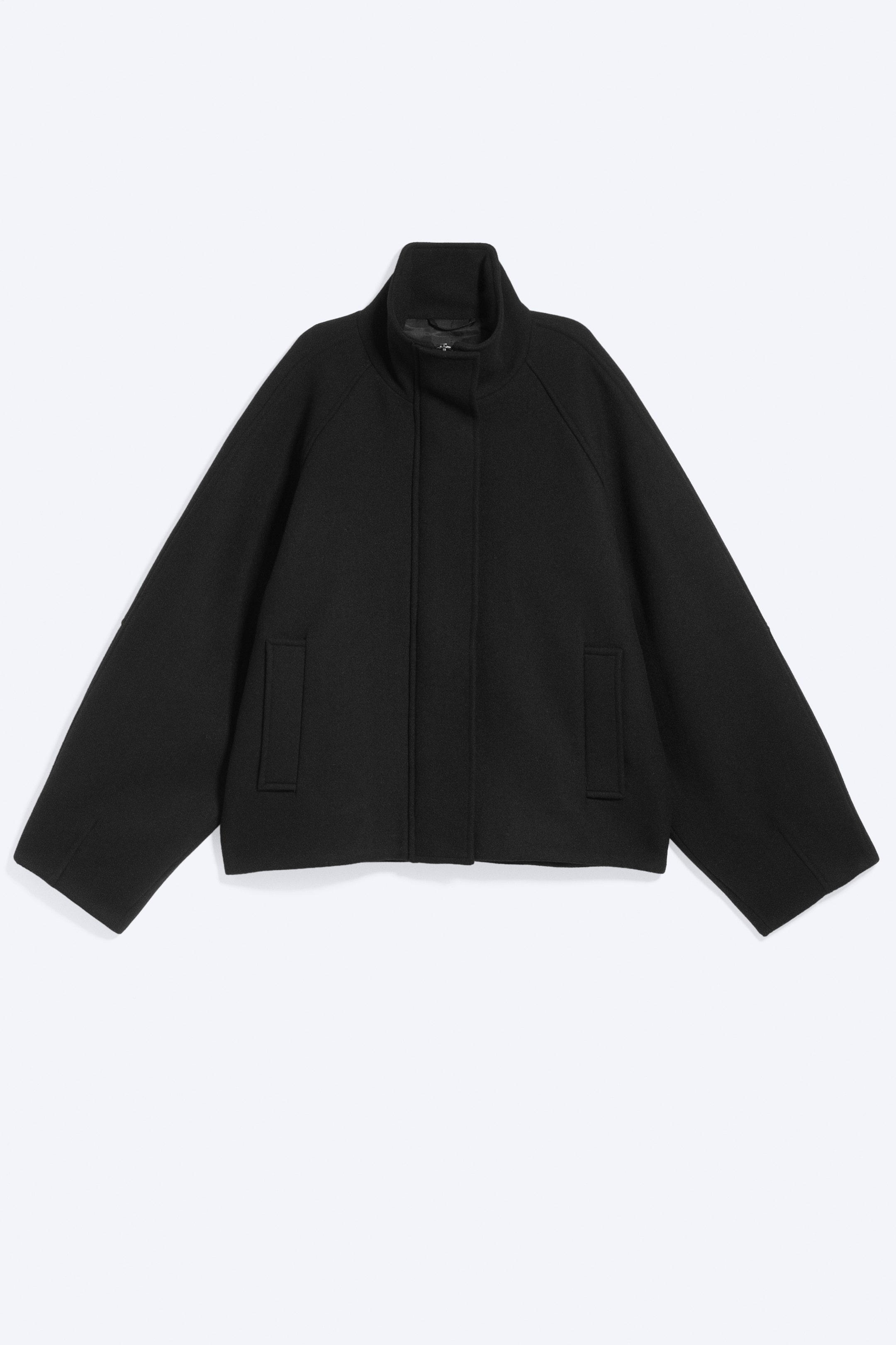 Grösseres Bild ansehen: Eine schwarze Wollmischungstrichterjacke präsentiert ihre Vorderseite, mit einem stehenden Trichterkragen und einer verdeckten Frontleiste. Sie ist mit weiten Raglanärmeln, zwei rechteckigen aufgesetzten Taschen an der Vorderseite und einer kurzen, kastigen Silhouette gestaltet.