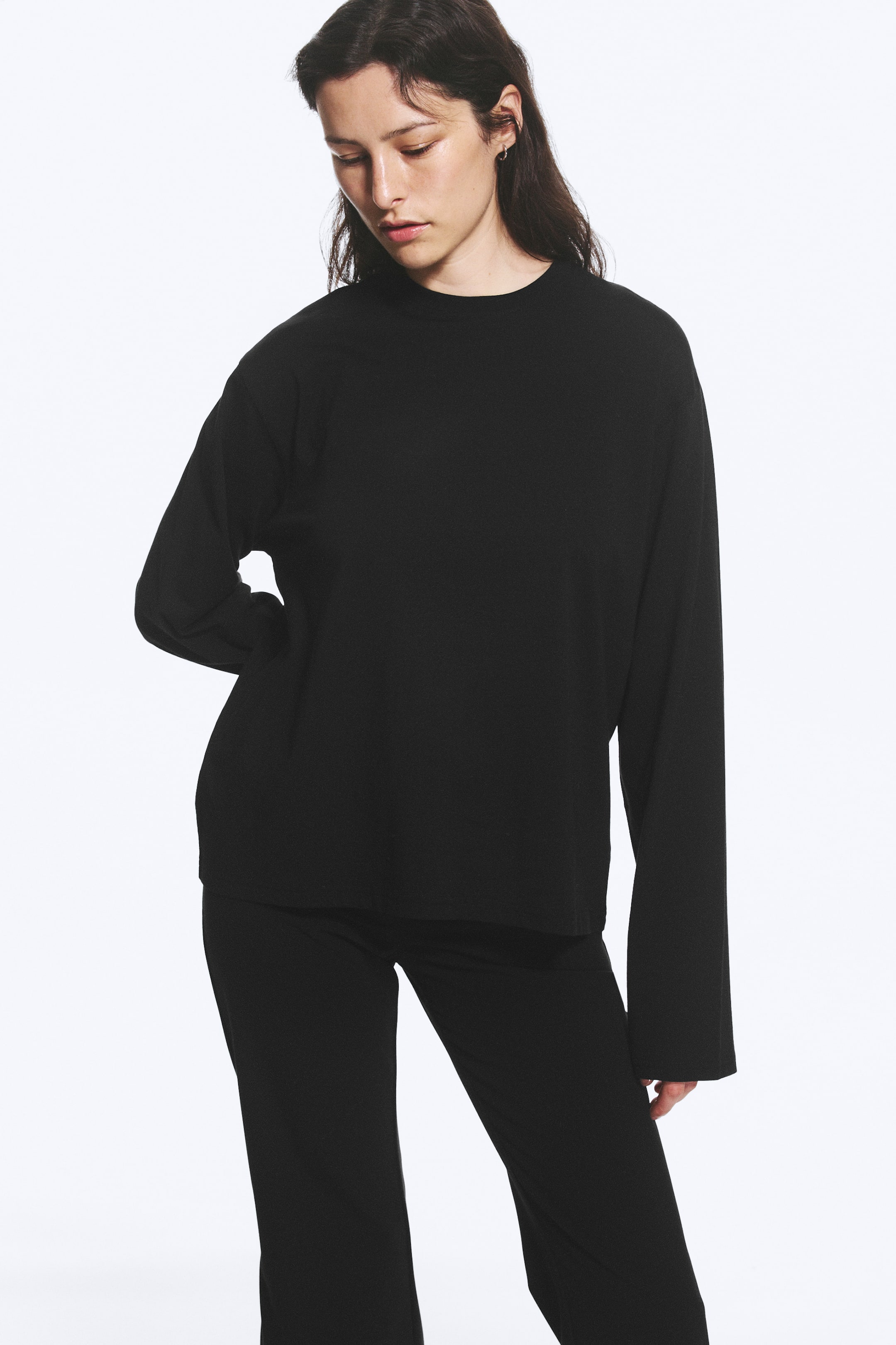 Agrandir l'image: Un haut noir à manches longues est présenté sous un angle avant-gauche, avec un col montant et une coupe décontractée. Il est associé à un pantalon noir à jambes larges.