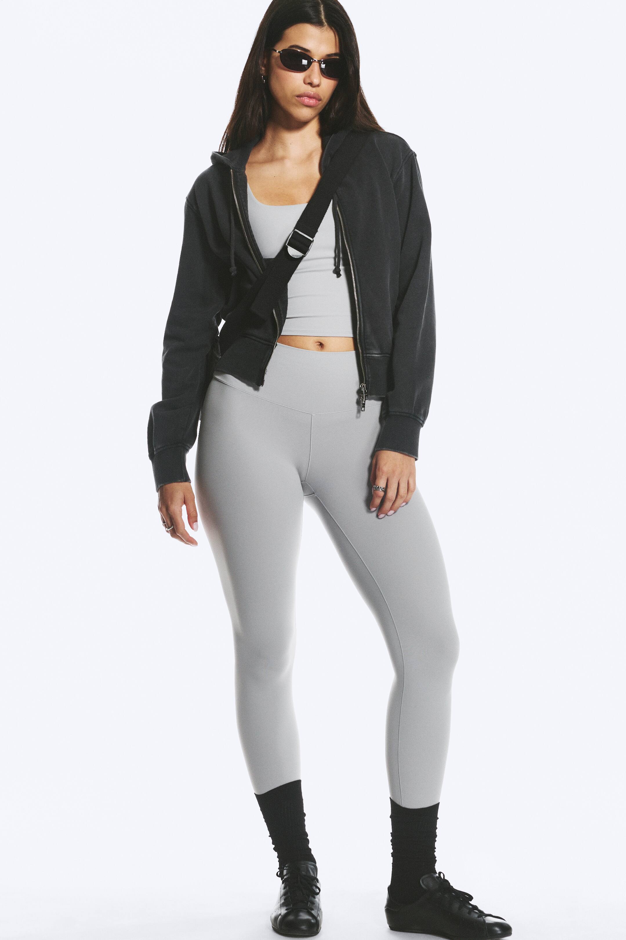Näytä suurempi kuva: Mallilla on yllään vaaleanharmaat, slim fit -malliset, täyspitkät urheilutrikoit, joissa on korkea ja leveä vyötärönauha. Vaaleanharmaa crop top on puettuna vyötärönauhan sisään, mikä korostaa korkeavyötäröistä muotoilua.