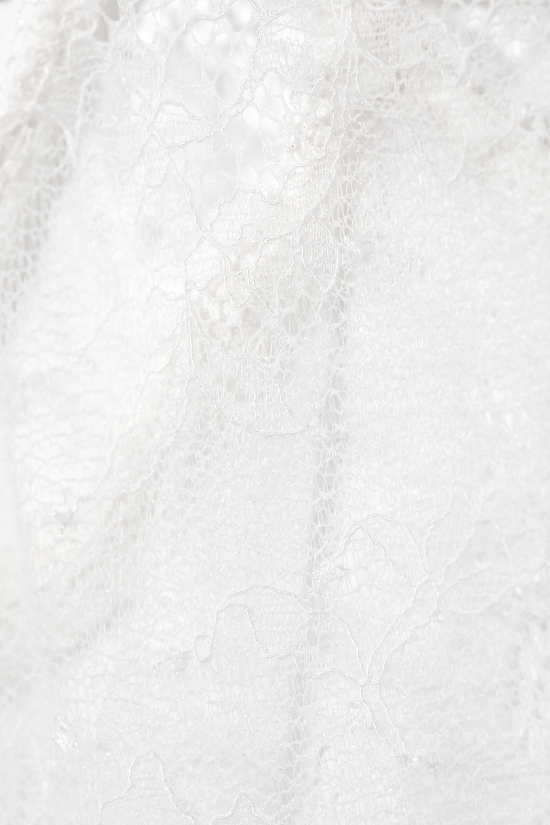 Ver imagen más grande: Una tela de encaje blanco muestra intrincados patrones florales con un delicado calado y una textura transparente.