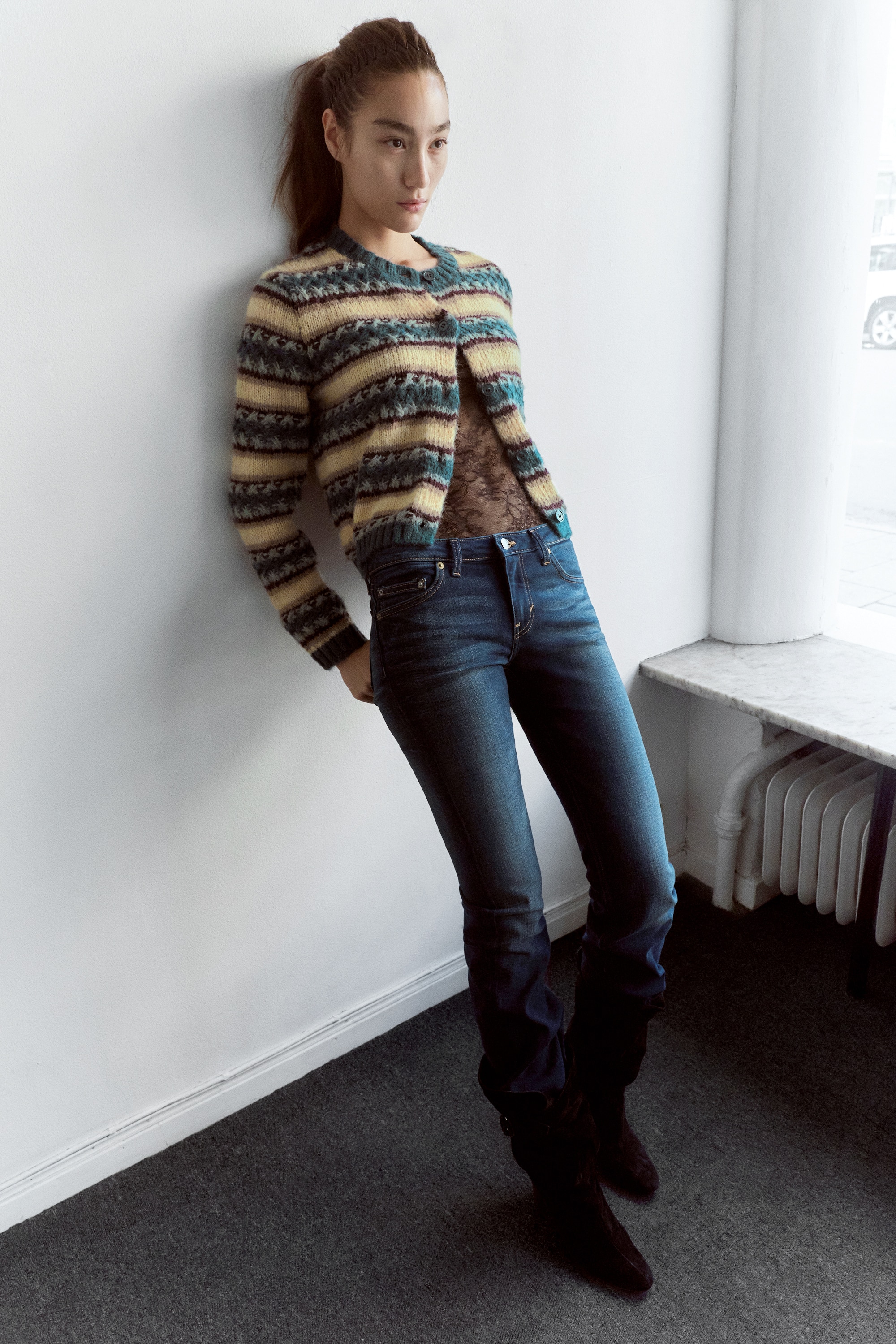 Un cardigan lavorato a maglia Ã¨ mostrato frontalmente, caratterizzato da un motivo a righe orizzontali all-over nei toni crema, teal e bordeaux. Ã progettato con girocollo, chiusura frontale con bottoni e finiture a coste teal coordinate su collo, polsini e orlo.