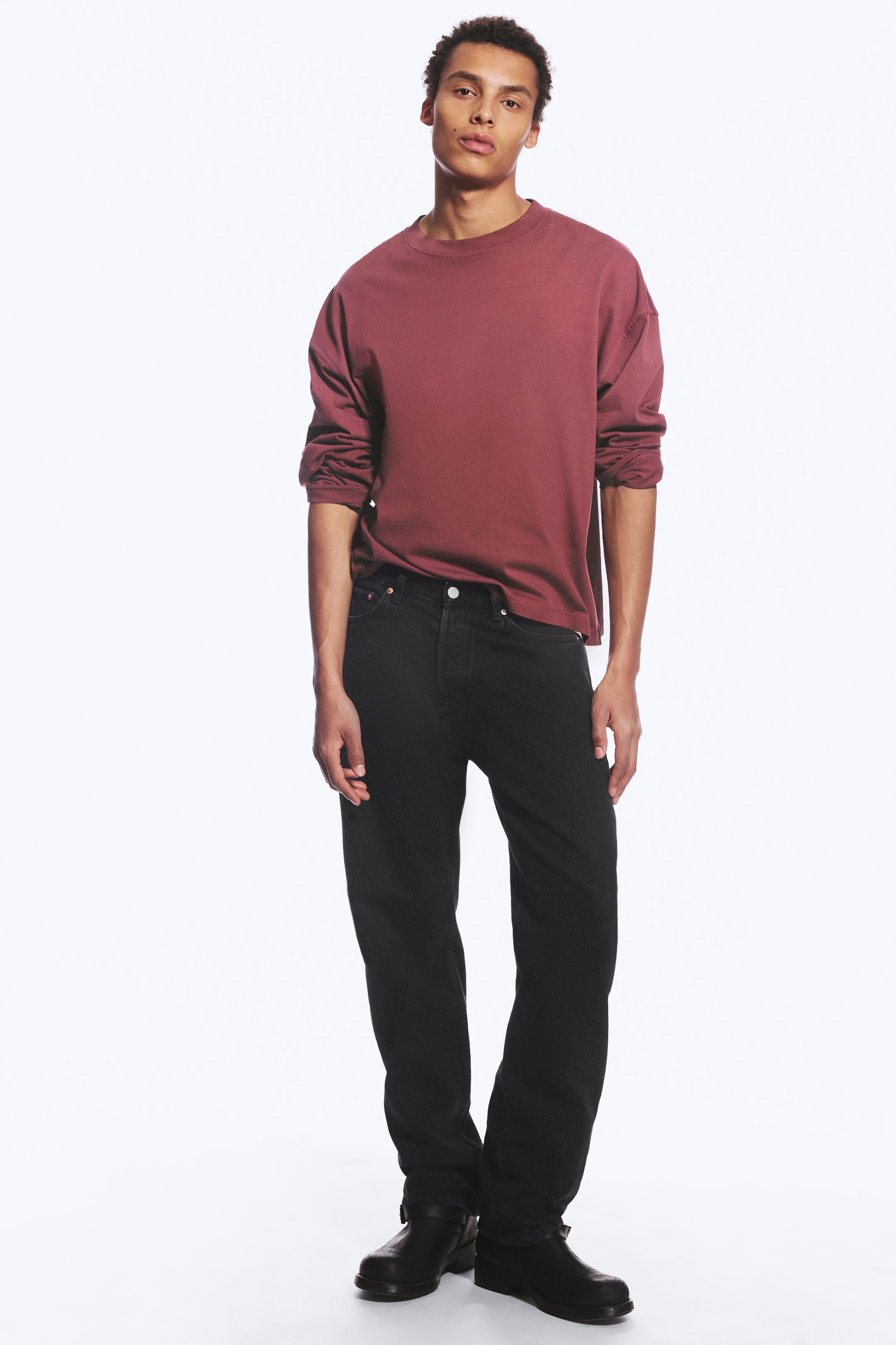 Ver imagen más grande: Los jeans negros de tiro medio, de corte relajado y pierna recta, los lleva la modelo, combinados con una camisa burdeos de manga larga y botas negras.