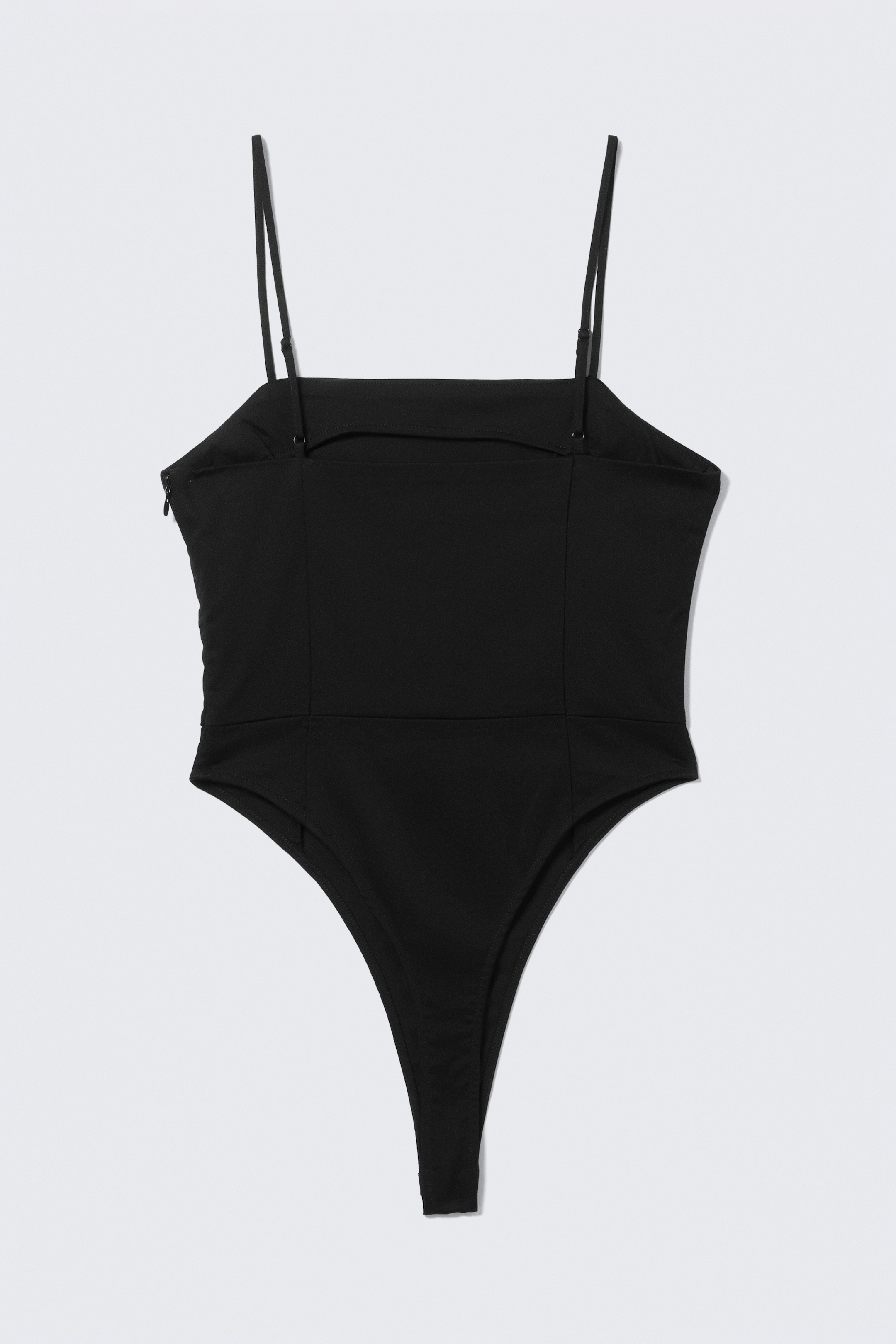 Ingrandisci l'immagine: Il body nero mostra il suo retro, con uno scollo dritto sulla schiena e sottili spalline regolabili. Presenta un design a gamba alta e una cerniera invisibile appare sul lato sinistro.