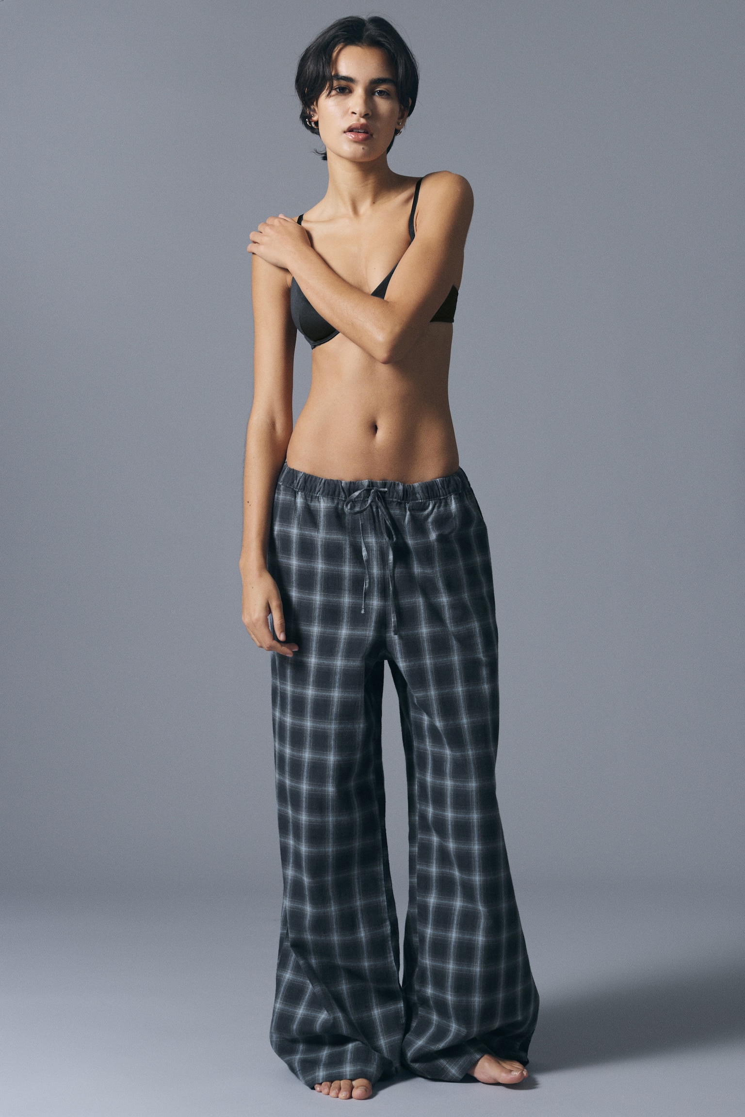 Vida flanellpyjamasbyxor i mörkgrått rutmönster bärs av modellen, med en mellanhög resårmidja med knytband i dragsko. Byxorna kombineras med en svart bh-topp. - 1