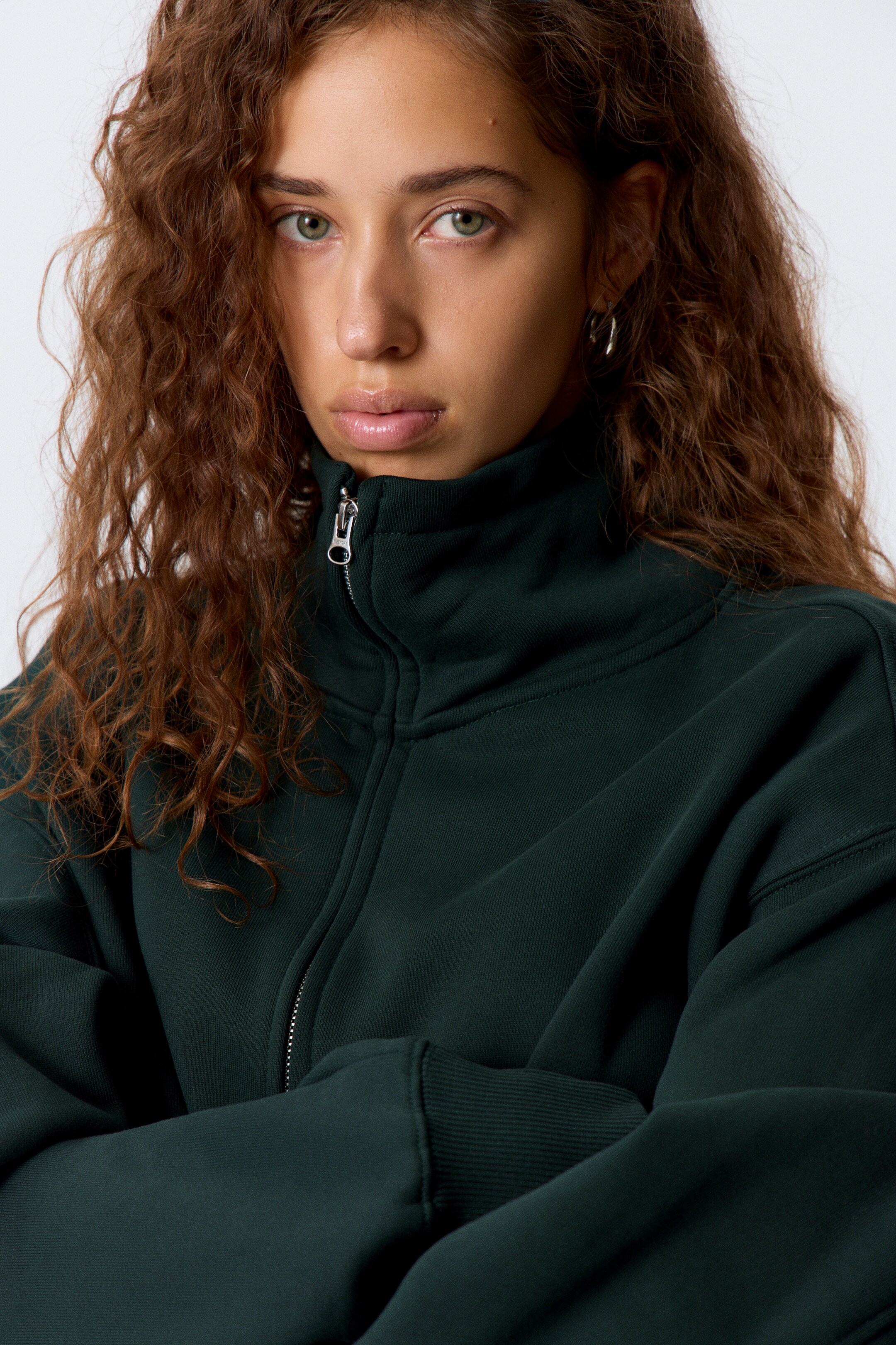 Visa större bild: En mörkgrön sweatshirt med hel dragkedja har en hög ståkrage med en delvis blixtlåst silverfärgad dragkedja, synlig framifrån. Sweatshirten har långa, avslappnade ärmar med ribbade muddar.