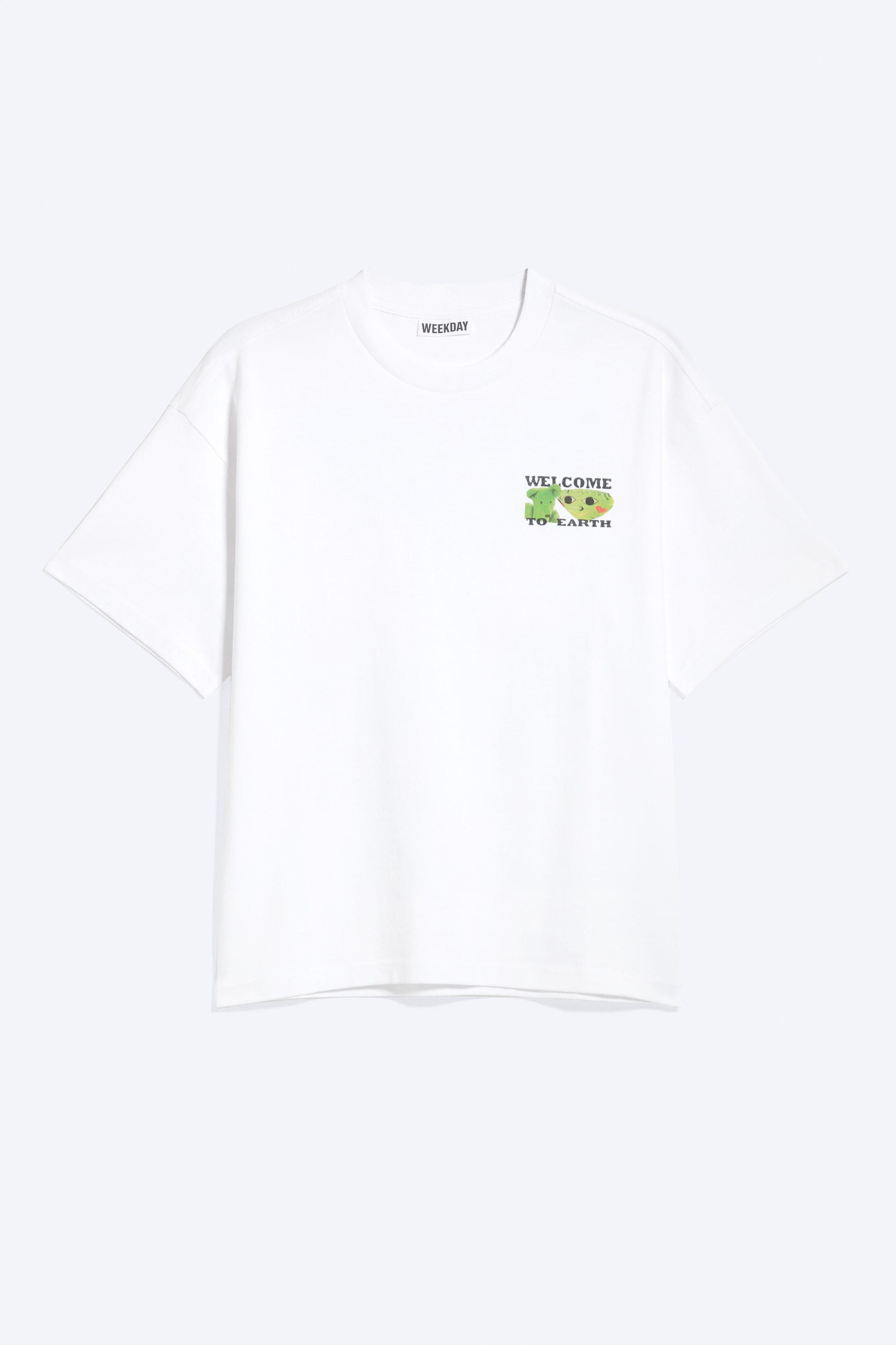 Grotere afbeelding bekijken: Een wit, loszittend t-shirt toont de voorkant, met een ronde halslijn, verlaagde schouders en een onafgewerkte zoom. Een grafisch ontwerp op de linkerborst toont twee groene alienfiguren naast de tekst "WELCOME TO EARTH".