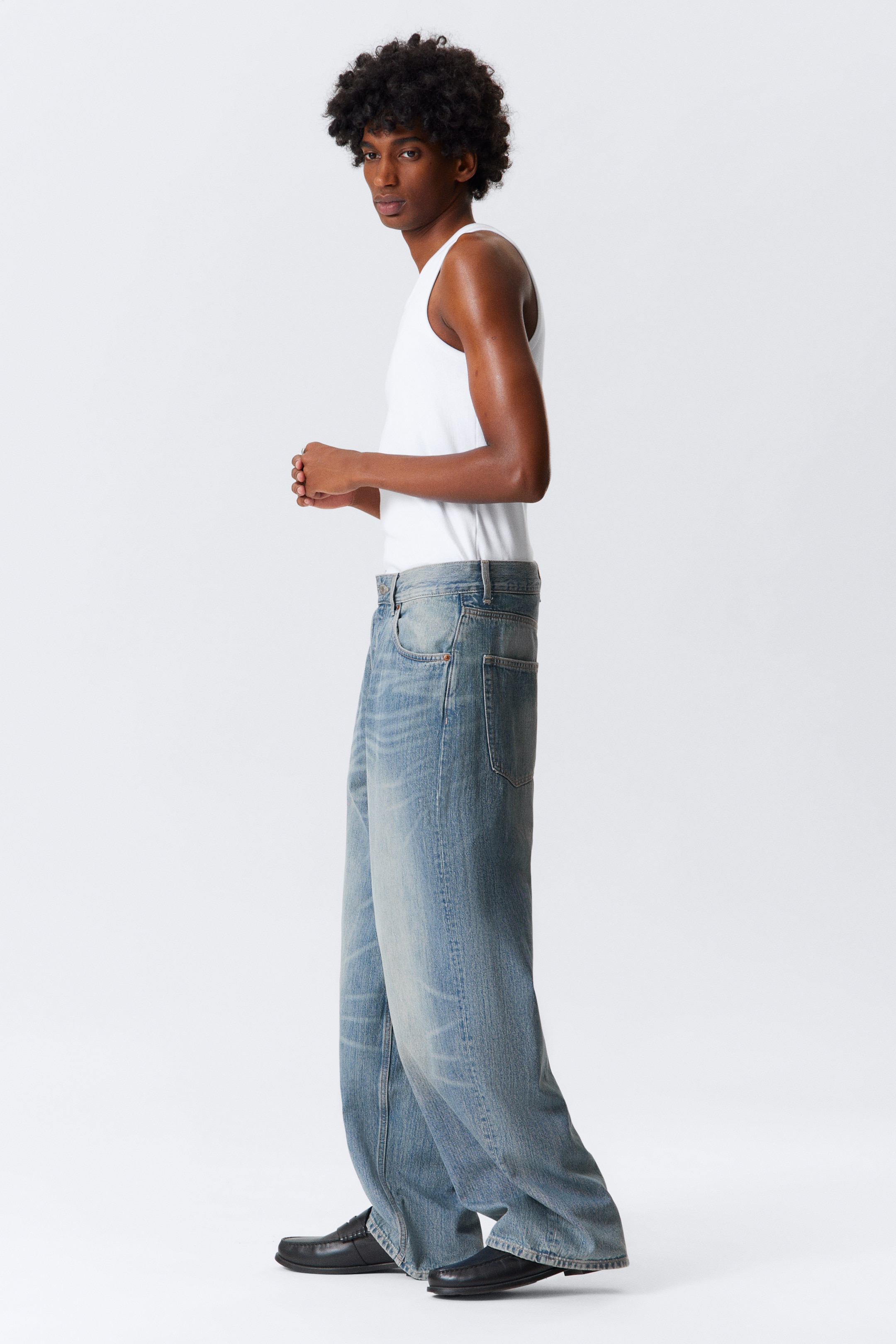 View larger image: Light blue, wide-leg jeans are being presented on a model, seen from the side, displaying a faded wash and pooling over black shoes at the hem. A white tank top is being worn tucked into the waistband of the jeans.