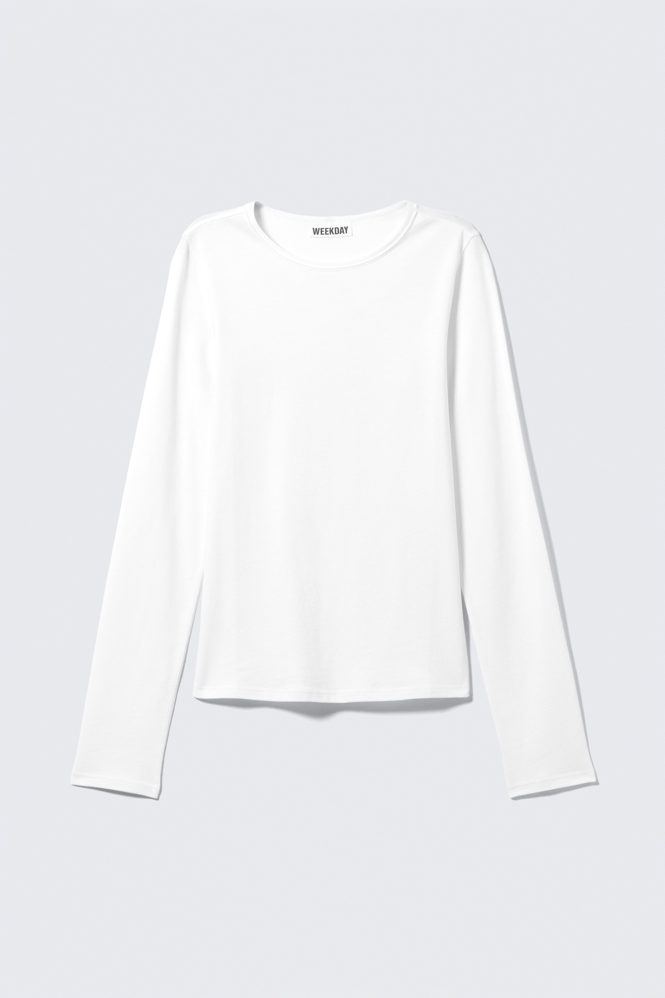 Agrandir l'image: Un haut à manches longues blanc est orienté vers l'avant, avec un col ras du cou et des manches longues. Le haut présente une texture de tissu lisse, et l'étiquette de la marque "WEEKDAY" est visible à l'intérieur de l'encolure arrière.