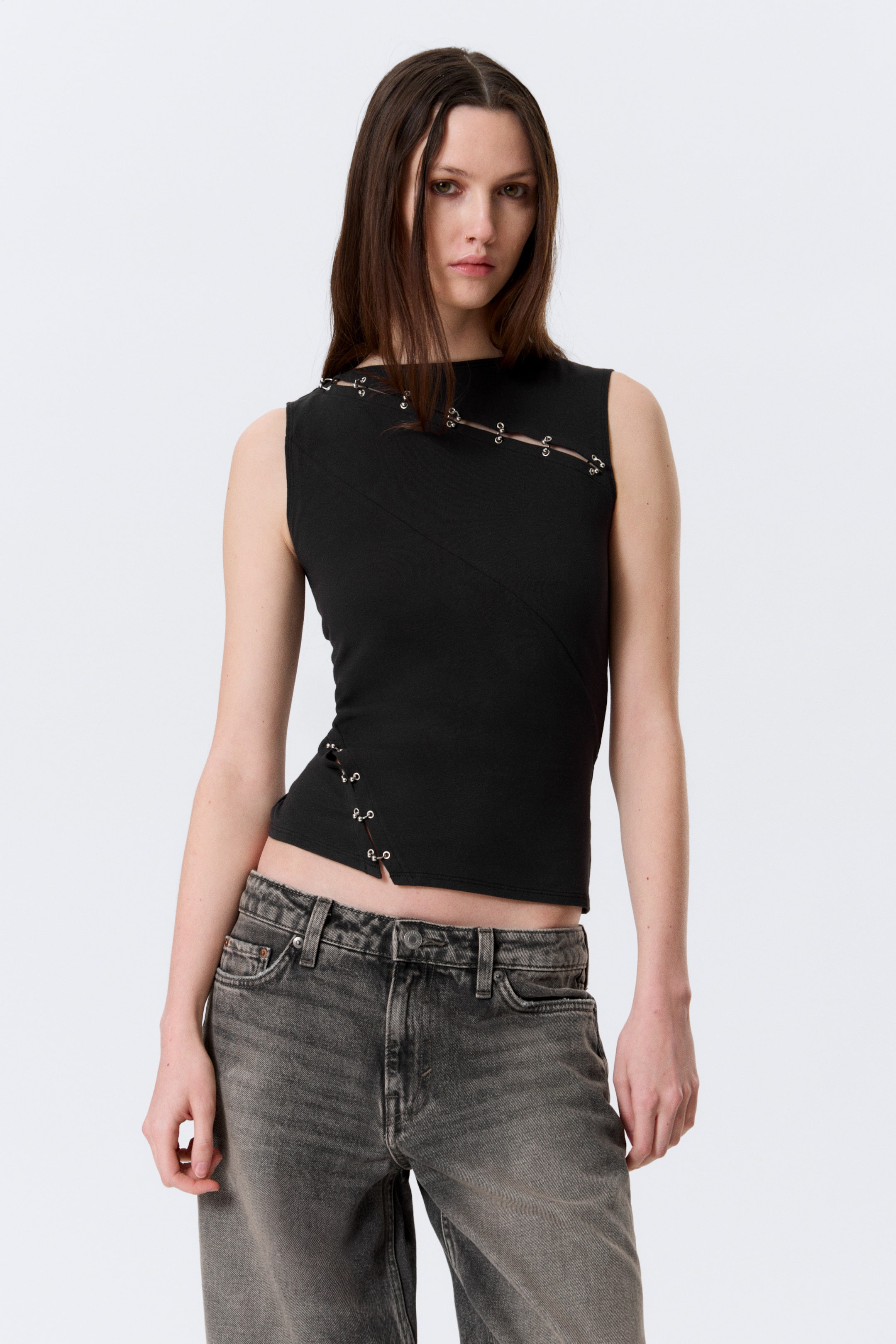 Ver imagen más grande: Un top negro sin mangas presenta un cuello alto. Un corte diagonal atraviesa el pecho y está asegurado con pequeños anillos plateados, mientras que otro corte diagonal aparece en el lado izquierdo, también sujeto con anillos plateados.
