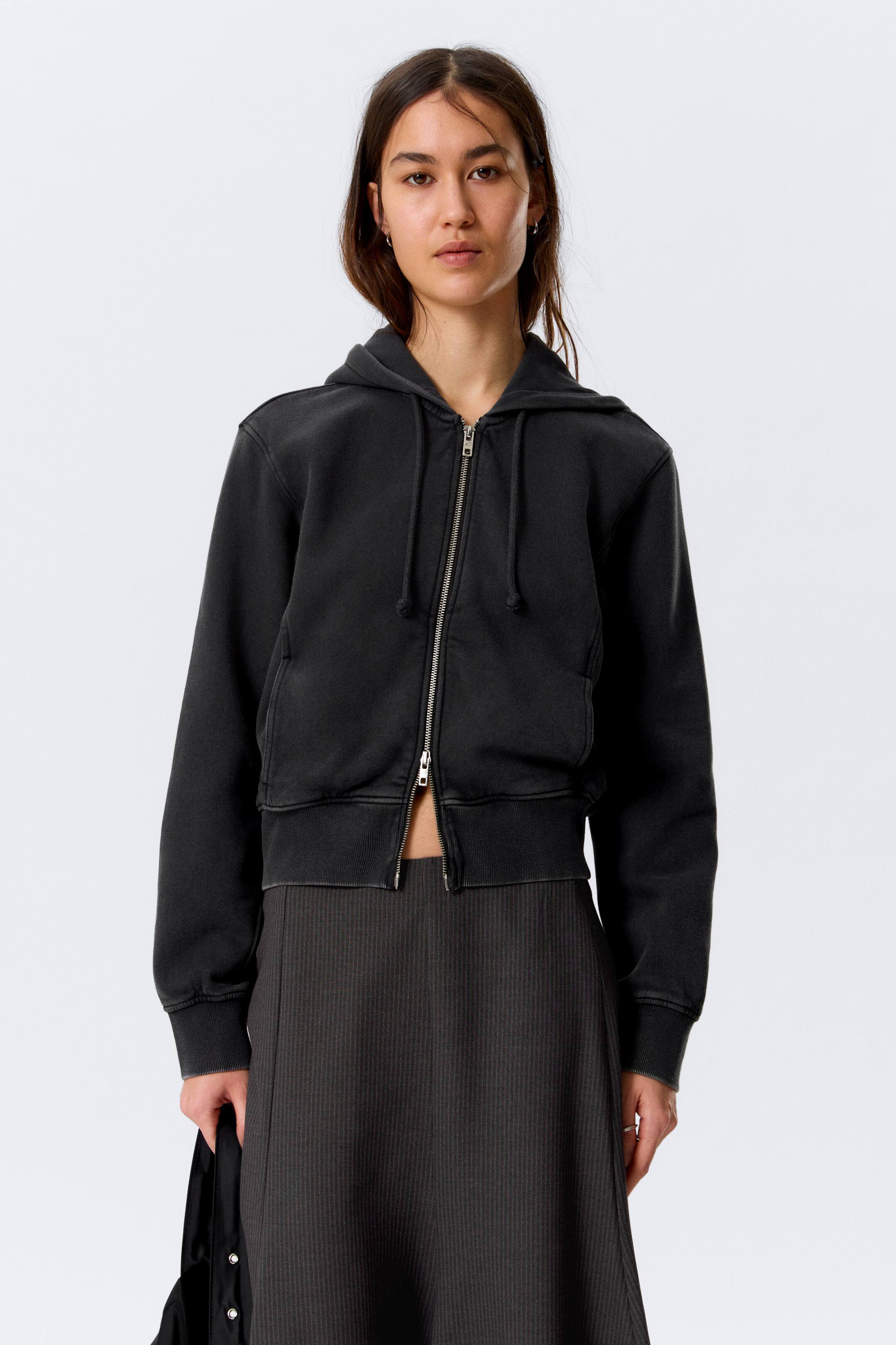 View larger image: A faded dark grey cropped hoodie is showcased from the front, featuring a partially unzipped silver full-zip closure, a hood with drawstrings, ribbed cuffs, and a ribbed hem. Subtle front pockets are visible on each side of the zip.