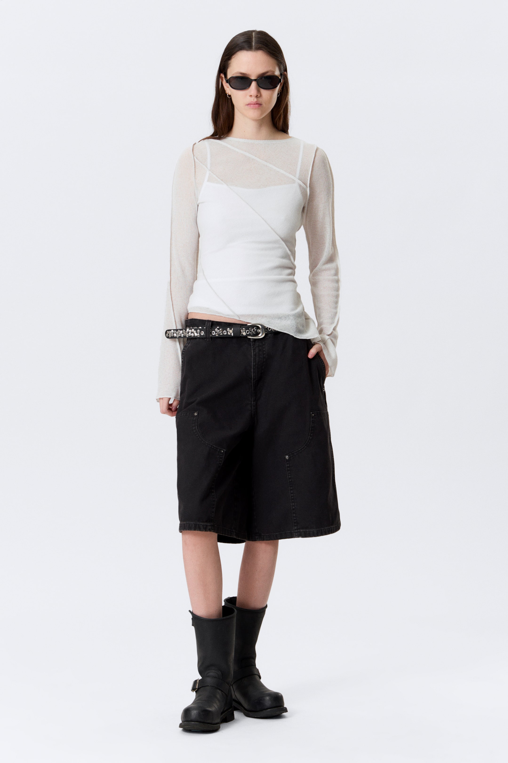 View larger image: The model is wearing a slim-fit sheer long-sleeved top over a white camisole. The top showcases a wide boat neckline, an asymmetric hemline, and cut-and-sewn seam detailing.