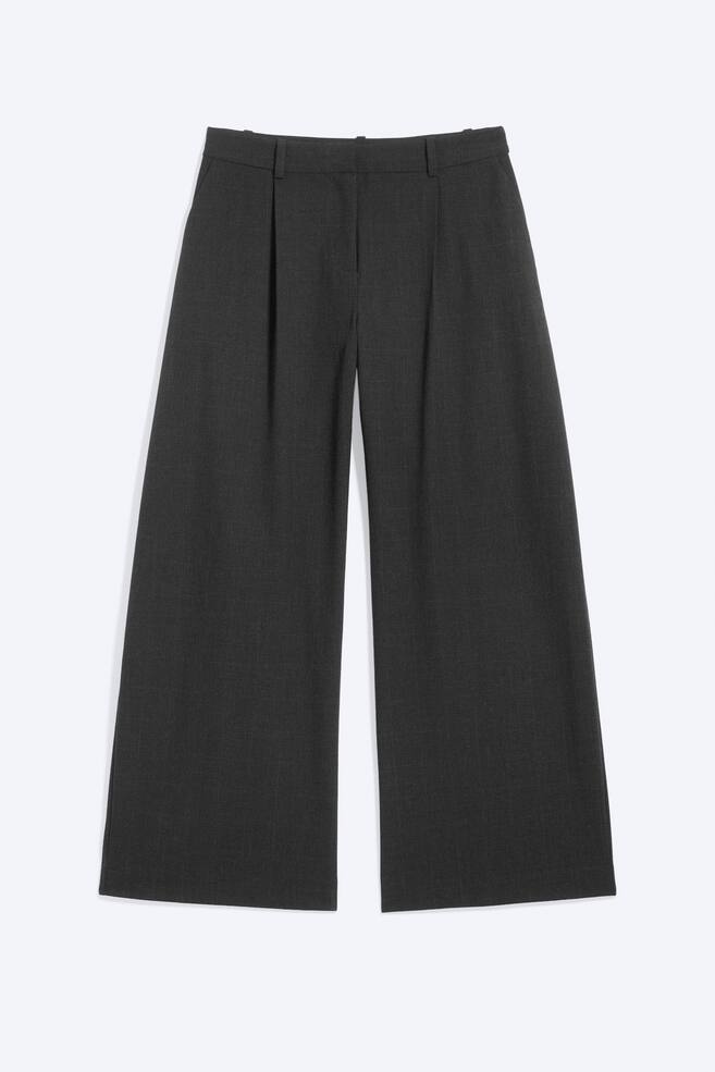 Se muestra un par de pantalones de traje de pierna ancha en gris oscuro, vistos de frente, con cintura con trabillas para cinturÃ³n, cierre frontal oculto y un solo pliegue delantero. Los pantalones caen en perneras amplias y holgadas con discretos bolsillos laterales inclinados. - 1