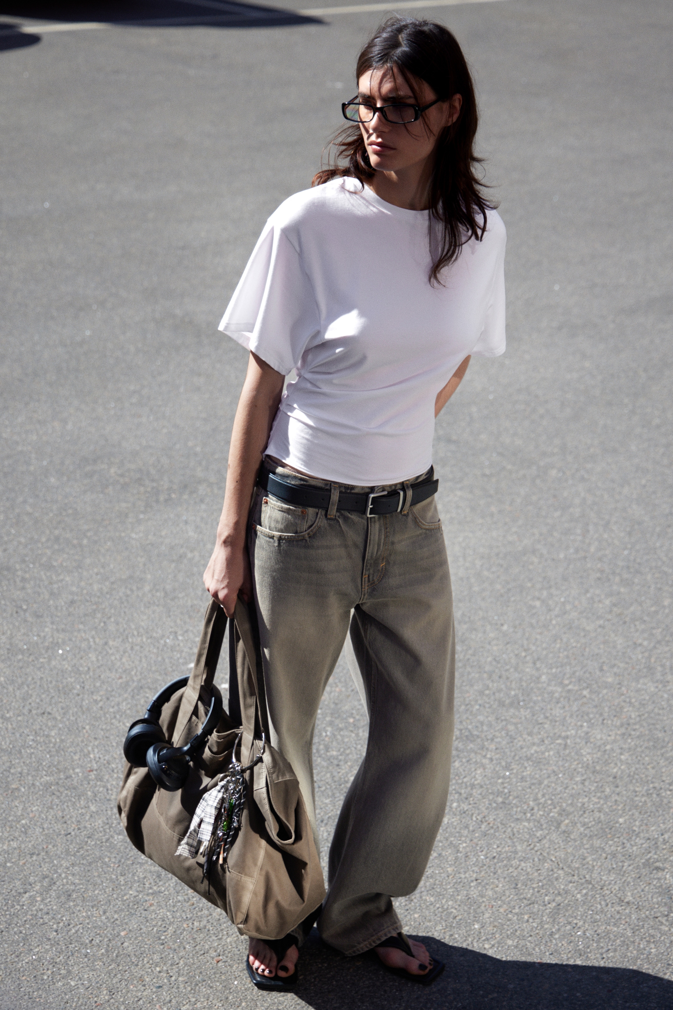View larger image: A white short-sleeved top is being worn, featuring a crew neck and loose, short sleeves. The fabric is gathering at the left side of the waist, creating a cinched, asymmetrical detail.