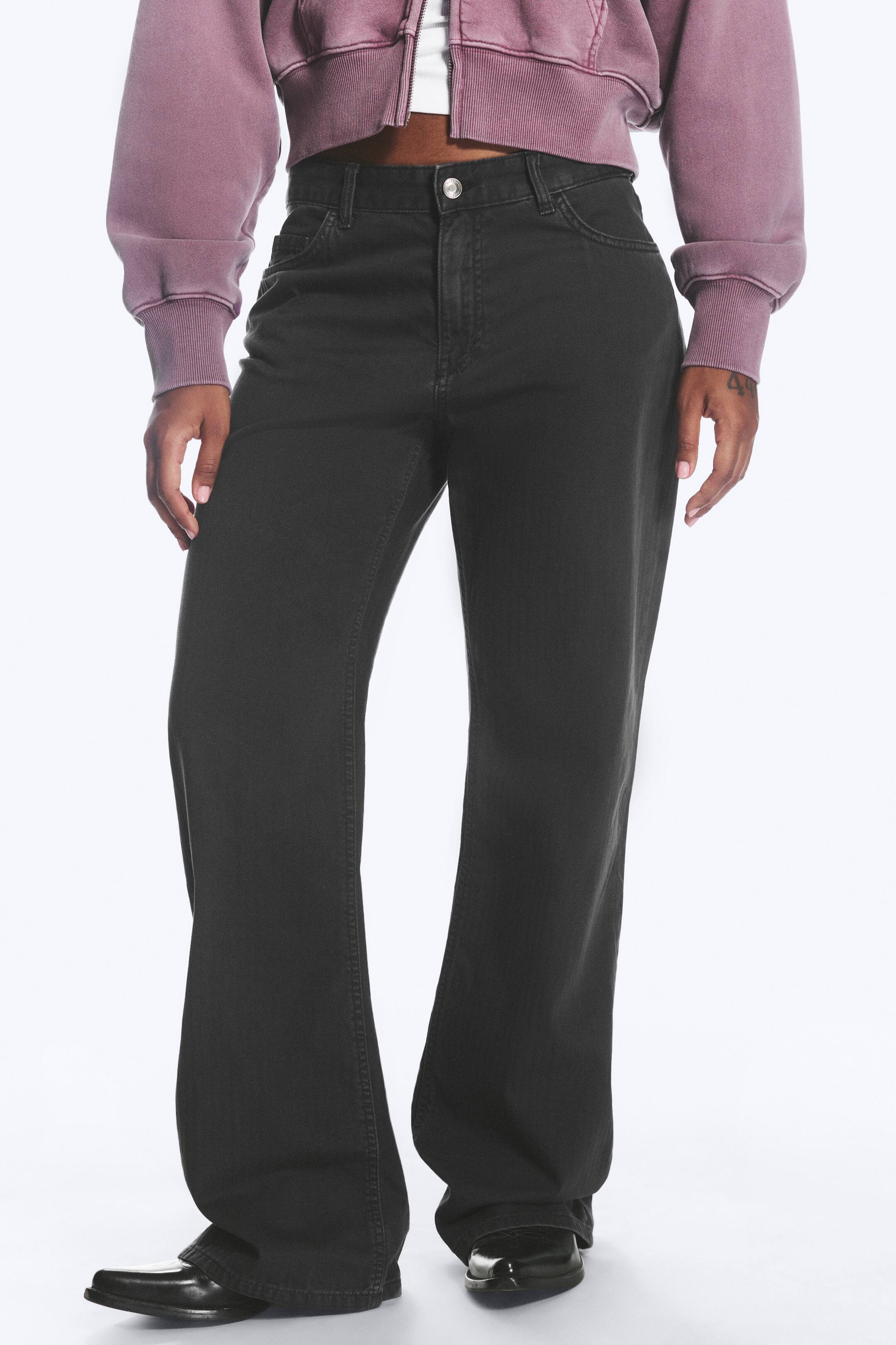 Agrandir l'image: Le mannequin porte un pantalon ample structuré de couleur gris foncé. Il présente une taille haute avec une fermeture à bouton et des poches avant, et les jambes tombent librement jusqu'au sol, recouvrant le dessus des chaussures noires du mannequin.