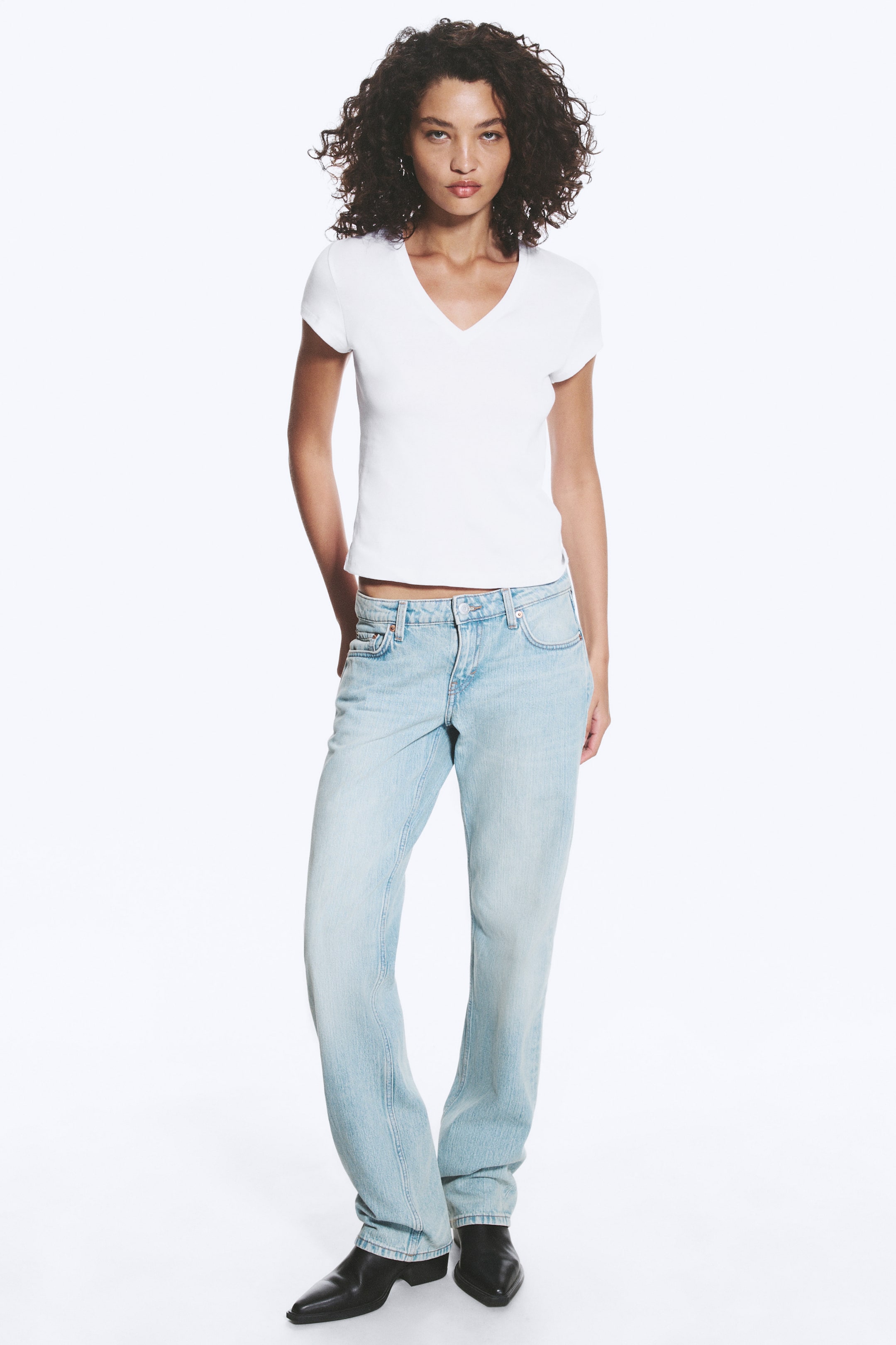 View larger image: A white V-neck T-shirt is showcasing a fitted silhouette with short sleeves and a slightly cropped hem, extending just above light-wash jeans.