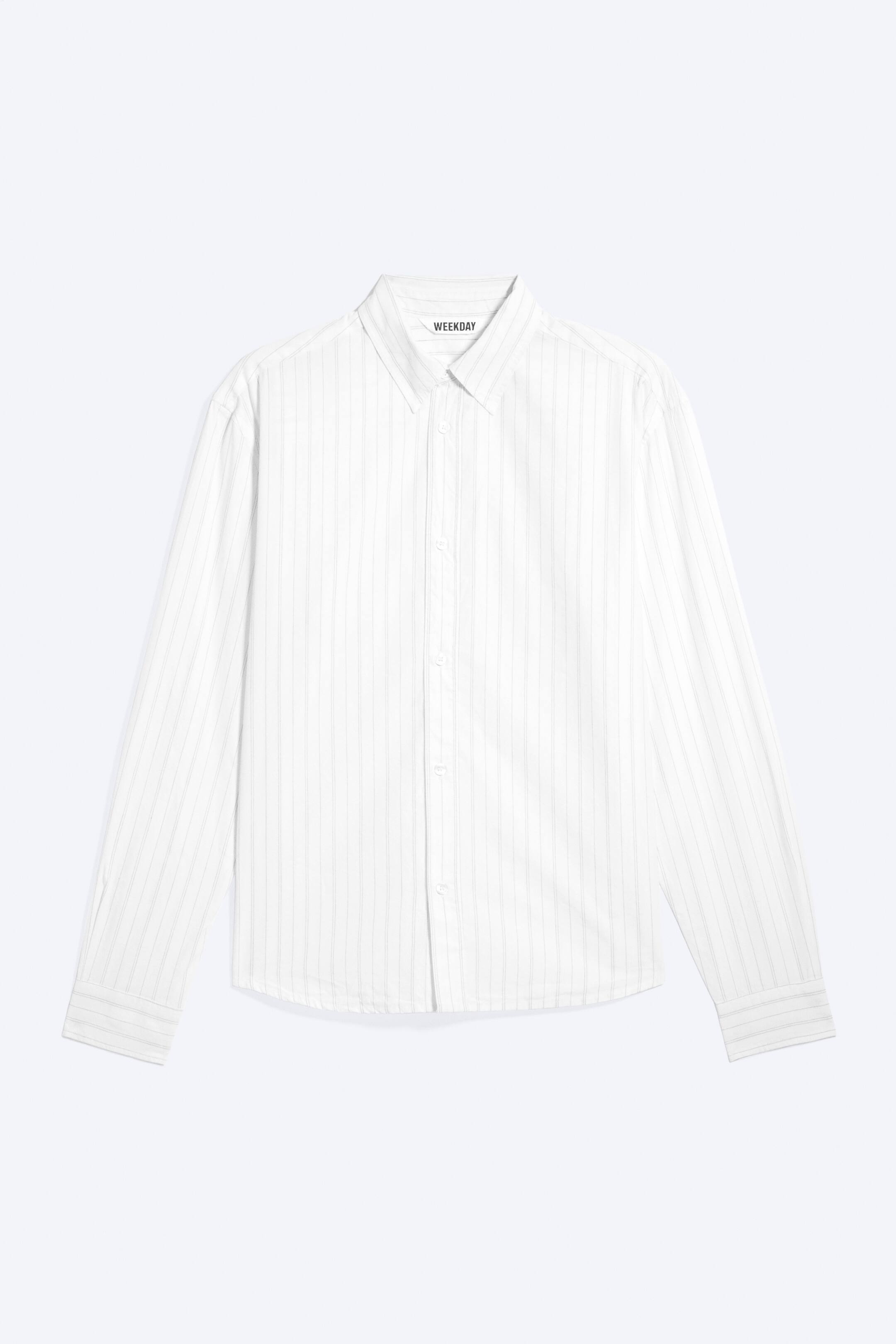 Ver imagem maior: Uma camisa branca de manga comprida é apresentada de frente, com finas riscas verticais cinzentas claras. Apresenta um colarinho pontiagudo, uma carcela de botões completa com botões brancos e punhos com botão, com a etiqueta da marca 'WEEKDAY' visível na gola interior.