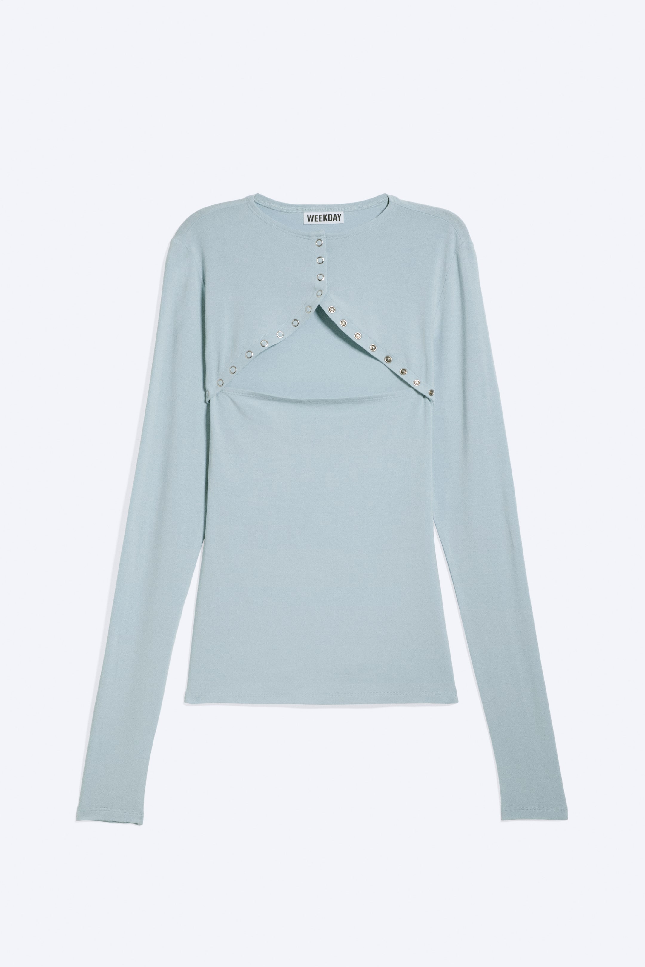 Visualizza immagine più grande: Un top a maniche lunghe azzurro chiaro è mostrato frontalmente, caratterizzato da uno scollo rotondo. Un overlay integrato in stile bolero crea un'apertura centrale sul petto, con occhielli color argento che decorano i bordi e si estendono fino al centro dello scollo anteriore.