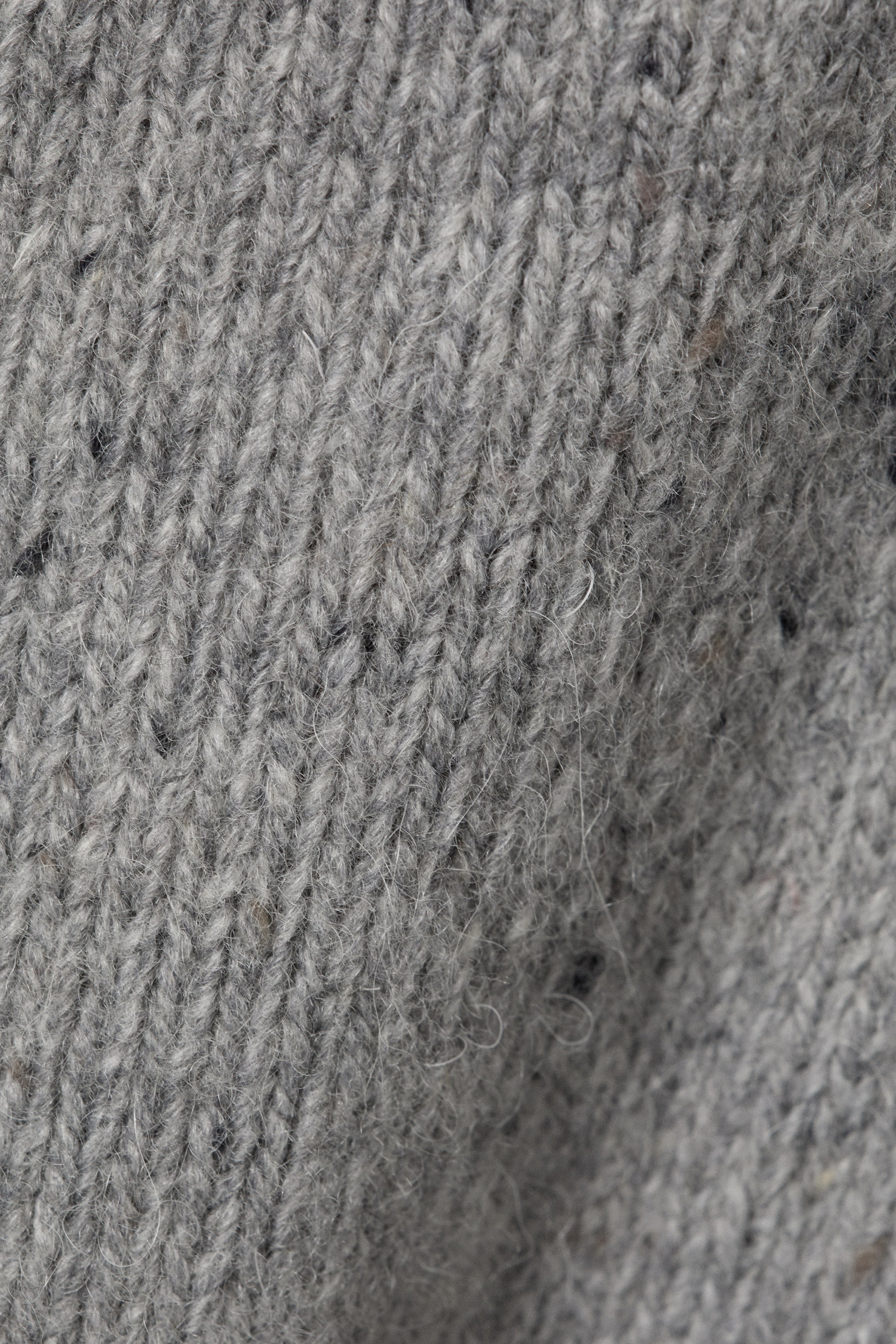 Agrandir l'image: Le tissu tricoté gris présente un motif de tricot uni avec des mailles en forme de V visibles. Il présente des petites taches sombres subtiles partout, créant une texture chinée et duveteuse.
