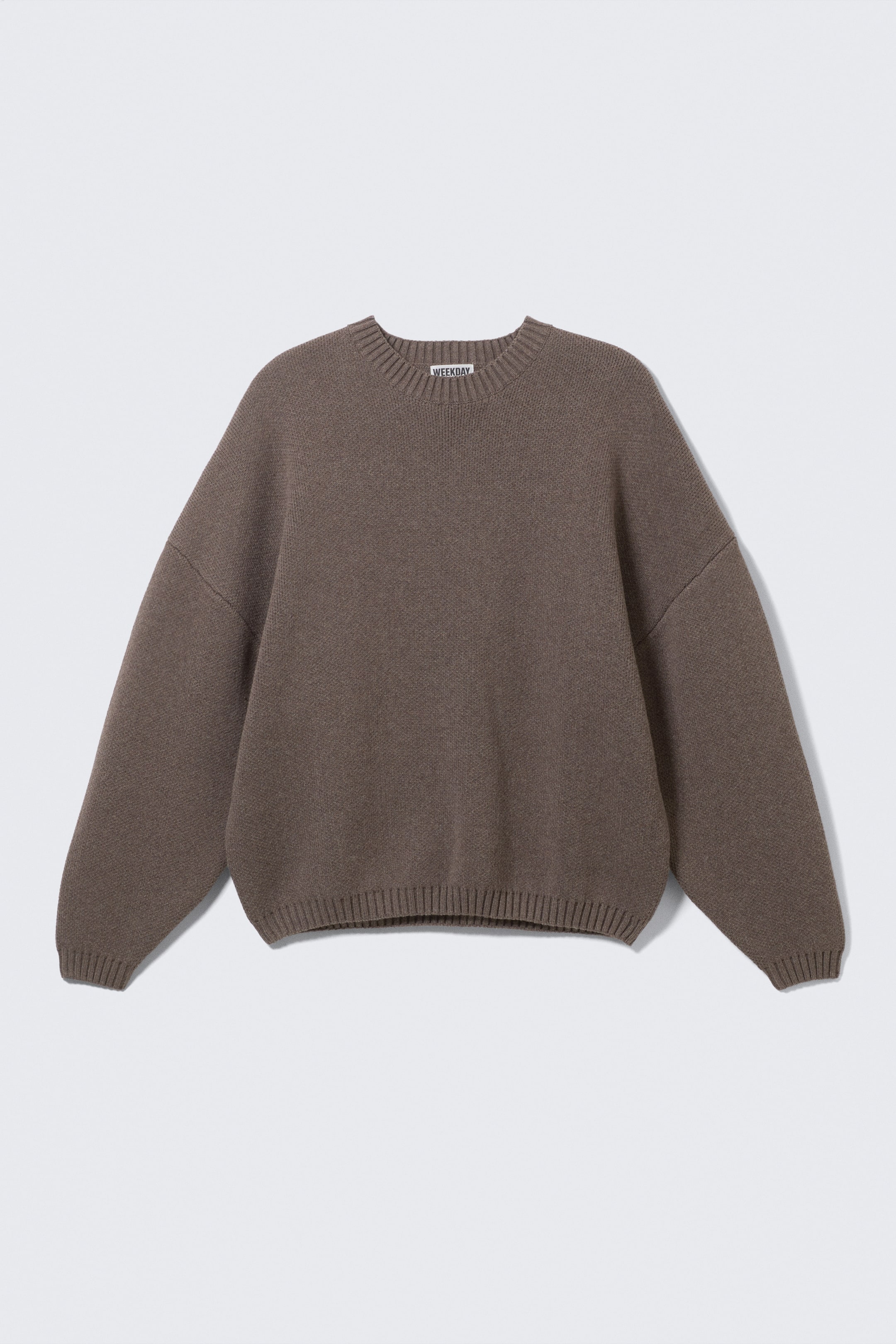 Visa större bild: En brun tjock tröja presenteras framifrån, med en oversized passform och nedhasade axlar. Den har en rund halsringning med en synlig 'WEEKDAY'-etikett, och ribbade kanter pryder hals, ärmslut och fåll.