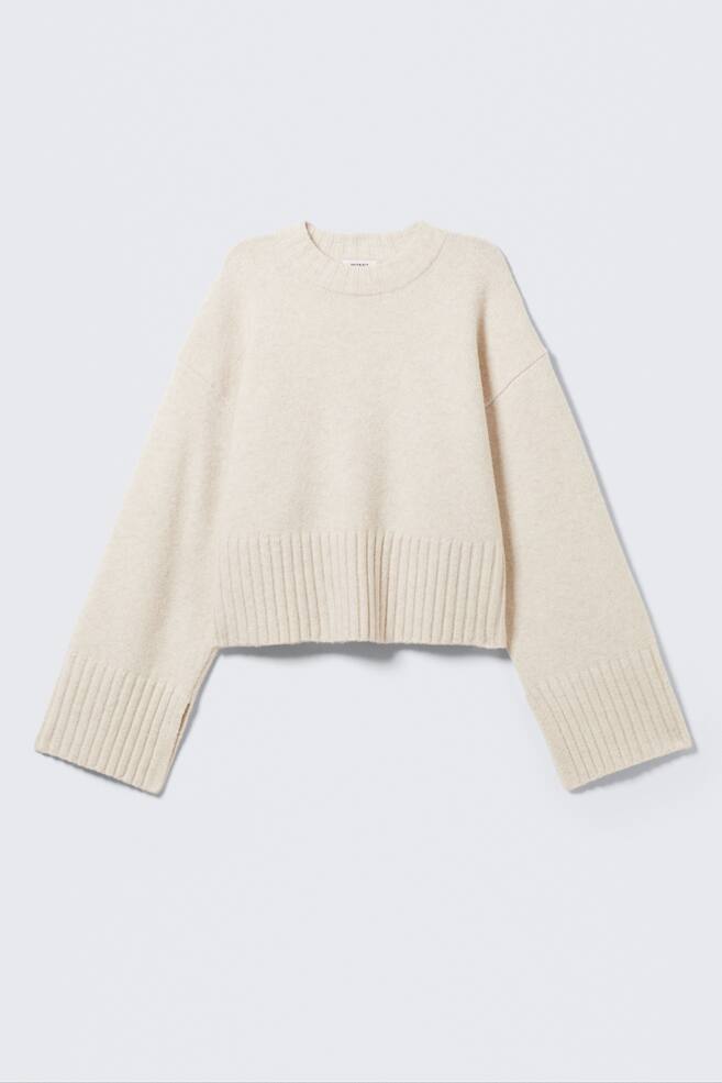 En ljusbeige stickad tröja presenteras FRAMIFRÅN, med en rund ribbad halsringning, vida långa ärmar med ribbade muddar och en liten yttre sidoslits, samt en ribbad fåll. - 1