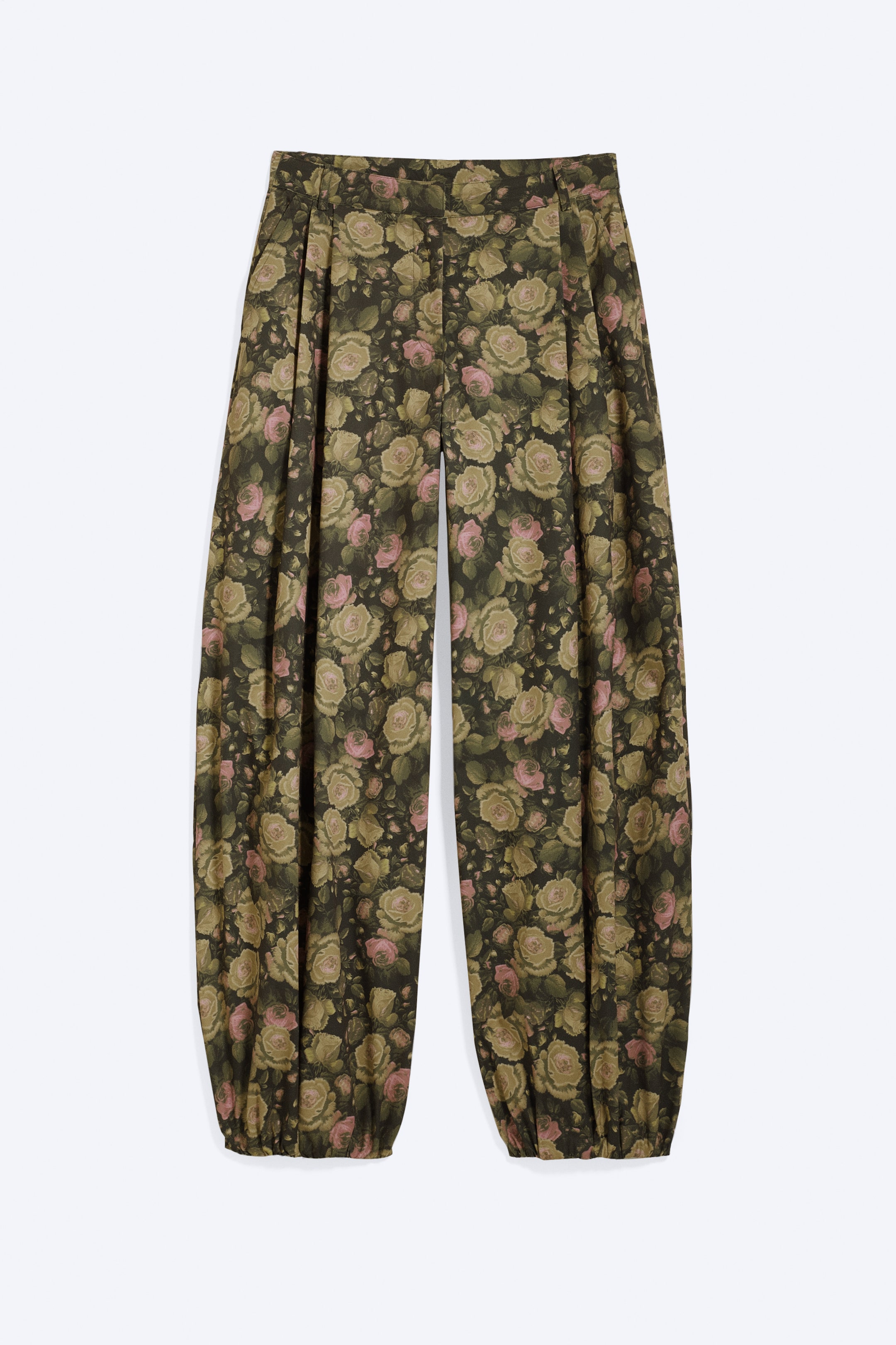 View larger image: A pair of oversized balloon trousers is shown from the front, featuring a dark green background with a floral pattern of pink and light green roses and olive leaves. The trousers are designed with a low-rise waist, voluminous legs, and finish at ankle length with gathered cuffs.