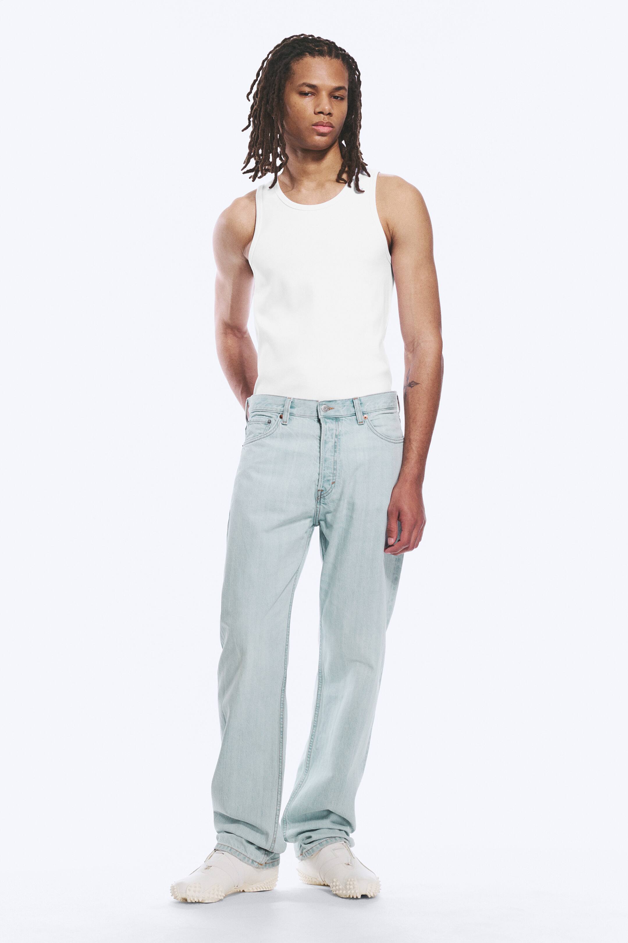 Se større billede: En hvid ribbet tanktop bæres, med en rund halsudskæring og en tætsiddende pasform. Lyse denimjeans bæres, med et lige ben, en synlig knaplukning og en afslappet pasform.