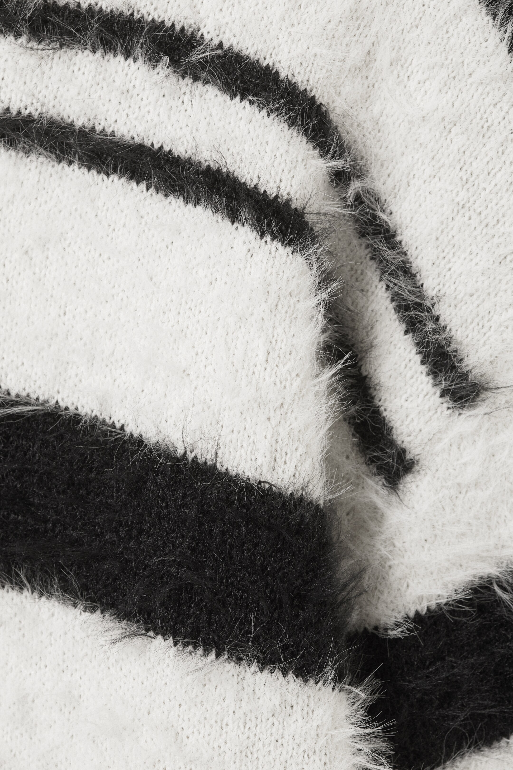 Visa större bild: Ett svartvitt stickat textilmaterial har breda, horisontella ränder med en distinkt luddig, raggig textur.