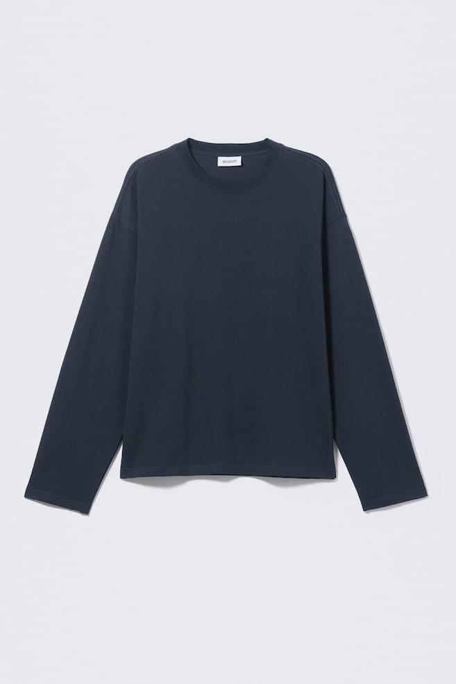 Una camiseta de manga larga azul oscuro está extendida, mostrando un cuello redondo y hombros caídos. Presenta un corte relajado y cuadrado con un dobladillo recto, y una pequeña etiqueta de la marca en blanco es visible en la parte interior del cuello trasero. - 1