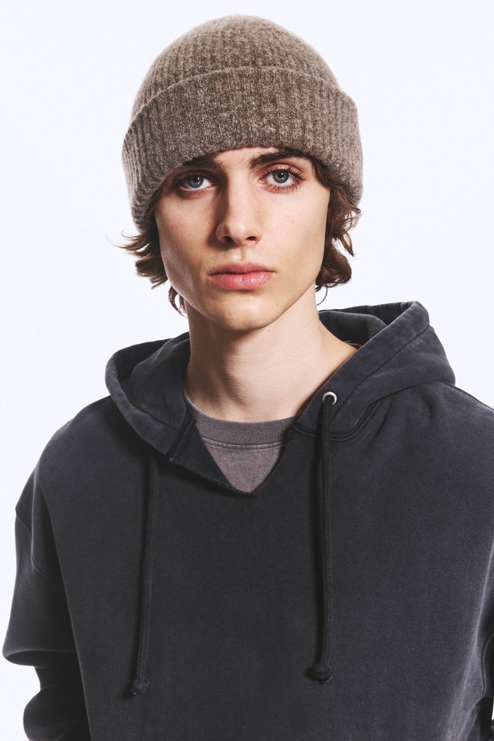 A knitted beanie in a textured brown mélange is shown from the front, featuring a close-fitting dome shape and a wide, folded ribbed turn-up.