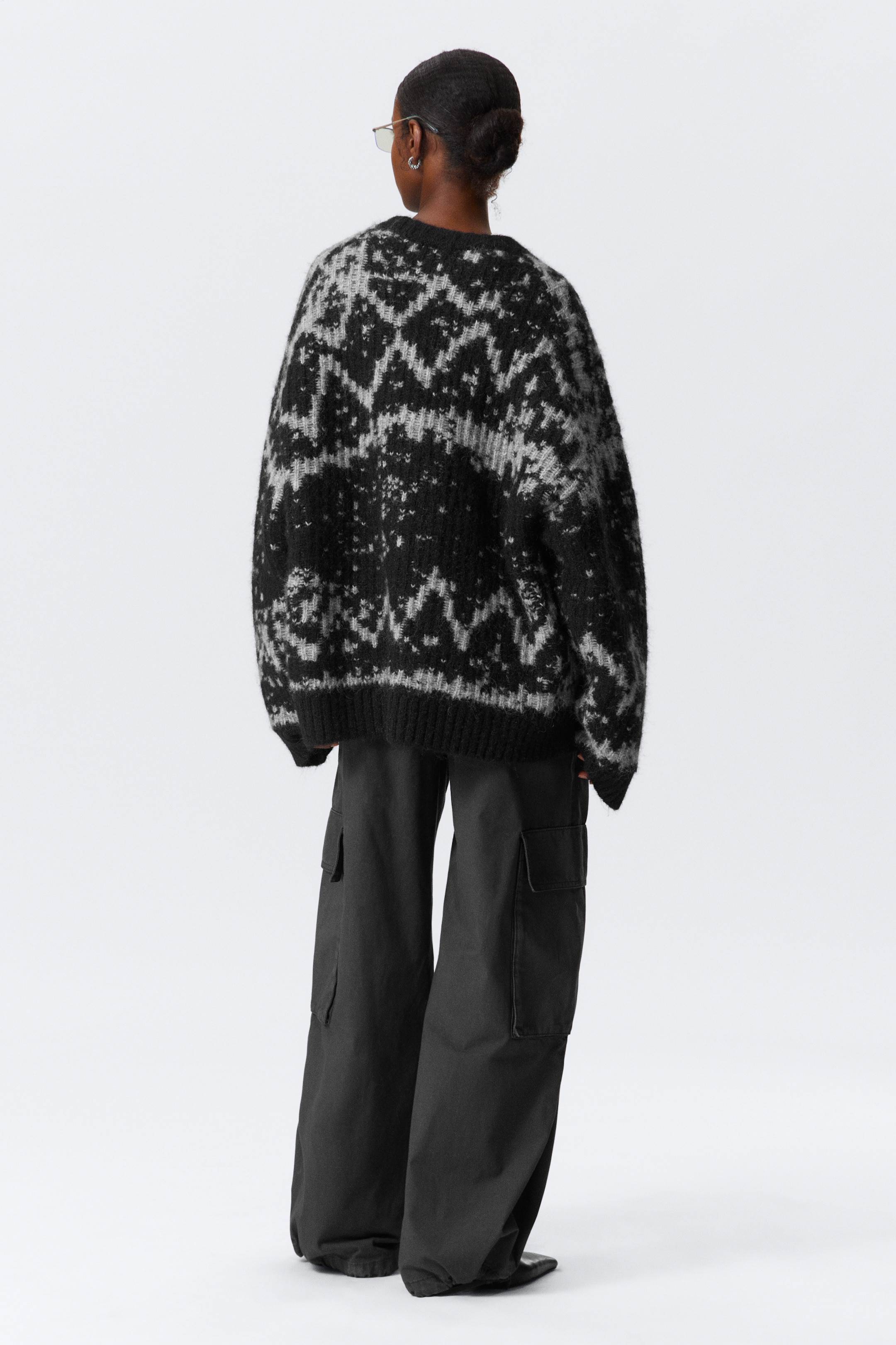 View larger image: An oversized black and grey fair isle sweater with a visible hairy texture is being worn by a model, viewed from the back. The relaxed fit sweater features a ribbed neckline, wide ribbed cuffs, and a wide ribbed hem, and is being styled with wide-leg black cargo pants.