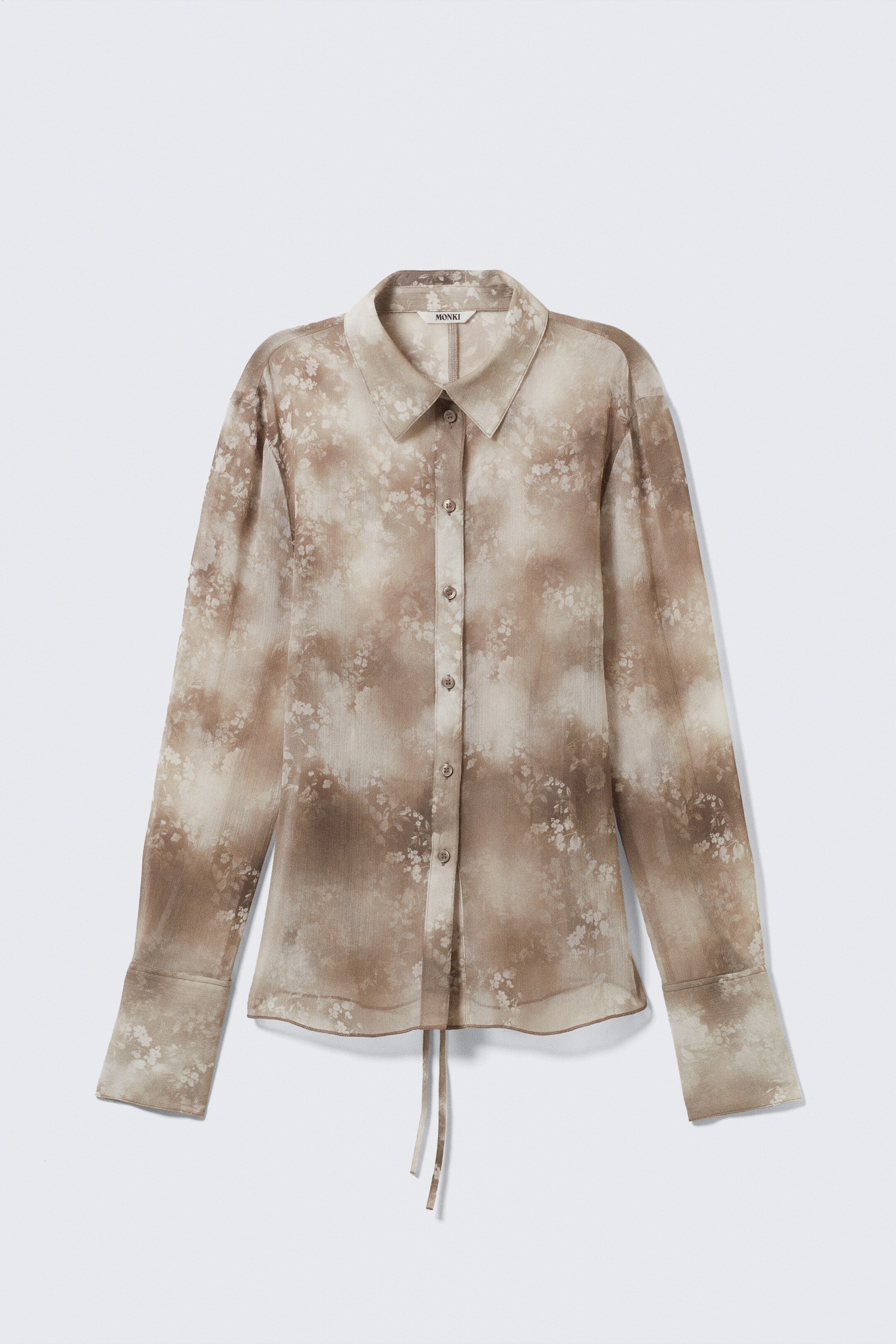 View larger image: A front view of a sheer long-sleeved shirt is showcasing a brown and beige watercolor-style floral pattern. It is featuring a pointed collar, a full-length button-front closure with brown buttons, and wide cuffs, with two thin ties hanging from its curved front hem.
