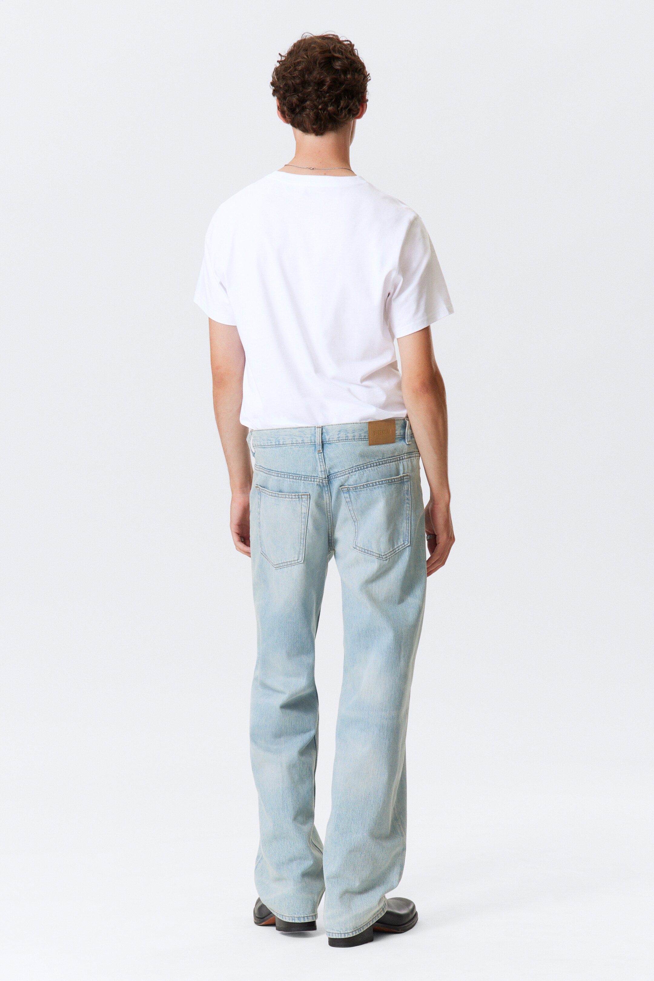 Visualizza immagine più grande: I jeans a lavaggio chiaro sono presentati da una vista posteriore, mettendo in mostra la loro vestibilità rilassata, a gamba dritta e il denim sbiadito azzurro. Presentano tasche posteriori visibili e una toppa marrone sul lato destro della cintura, mentre vengono indossati per dimostrare il loro drappeggio e la lunghezza.