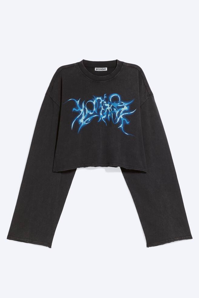 A faded black cropped long-sleeved T-shirt is shown from the front, featuring an oversized, boxy silhouette with dropped shoulders and extra-wide sleeves. The shirt displays a blue abstract graphic printed on the chest, a ribbed crew neckline, and raw-edge hems. - 1