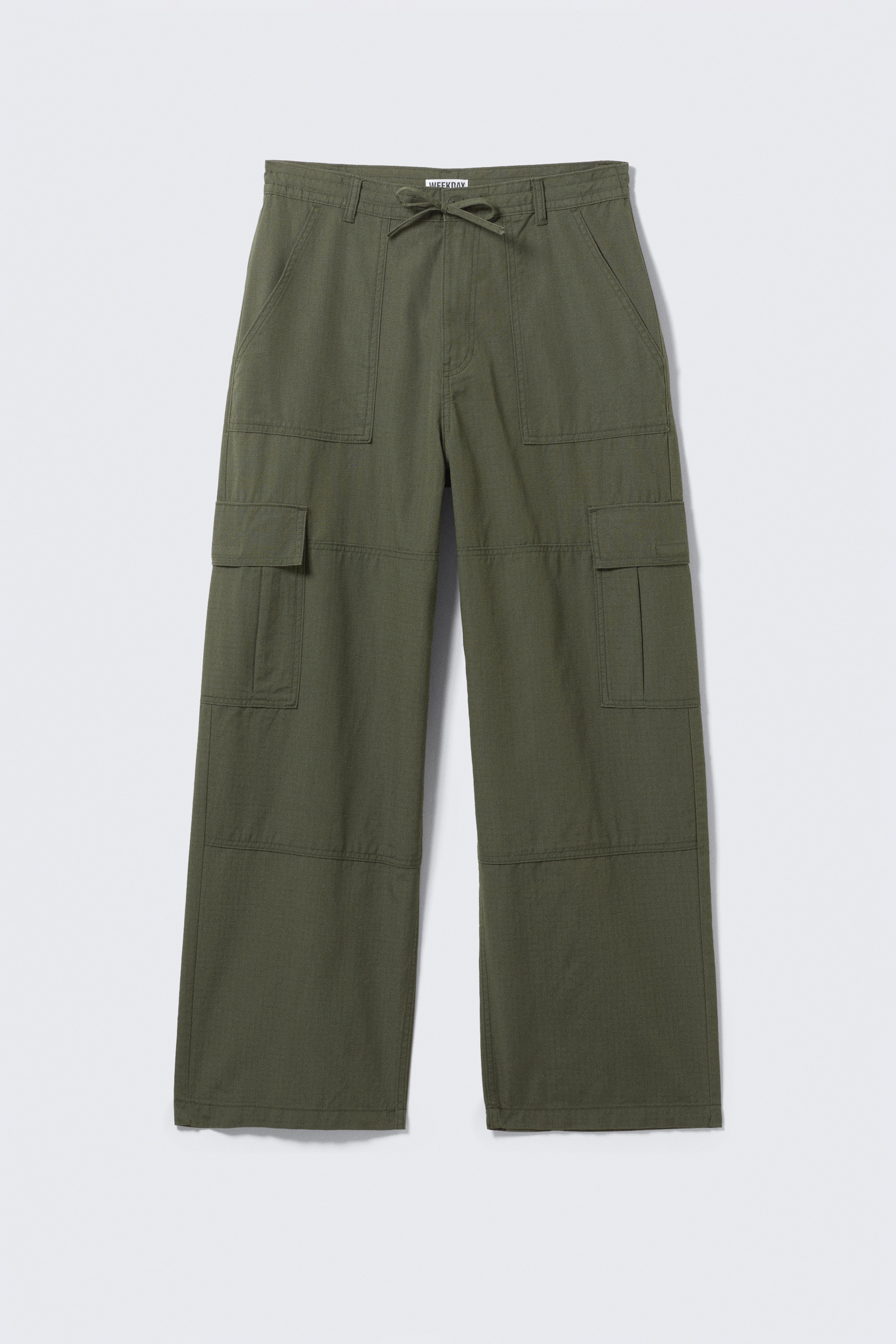 Visualizza immagine più grande: Un paio di pantaloni cargo verde oliva viene presentato, rivolto in avanti, mostrando una vestibilità ampia. Presentano una cintura con coulisse annodata a fiocco, passanti per cintura, chiusura con bottone, due tasche laterali oblique, due grandi tasche cargo a patta sulle cosce e cuciture articolate sulle ginocchia.