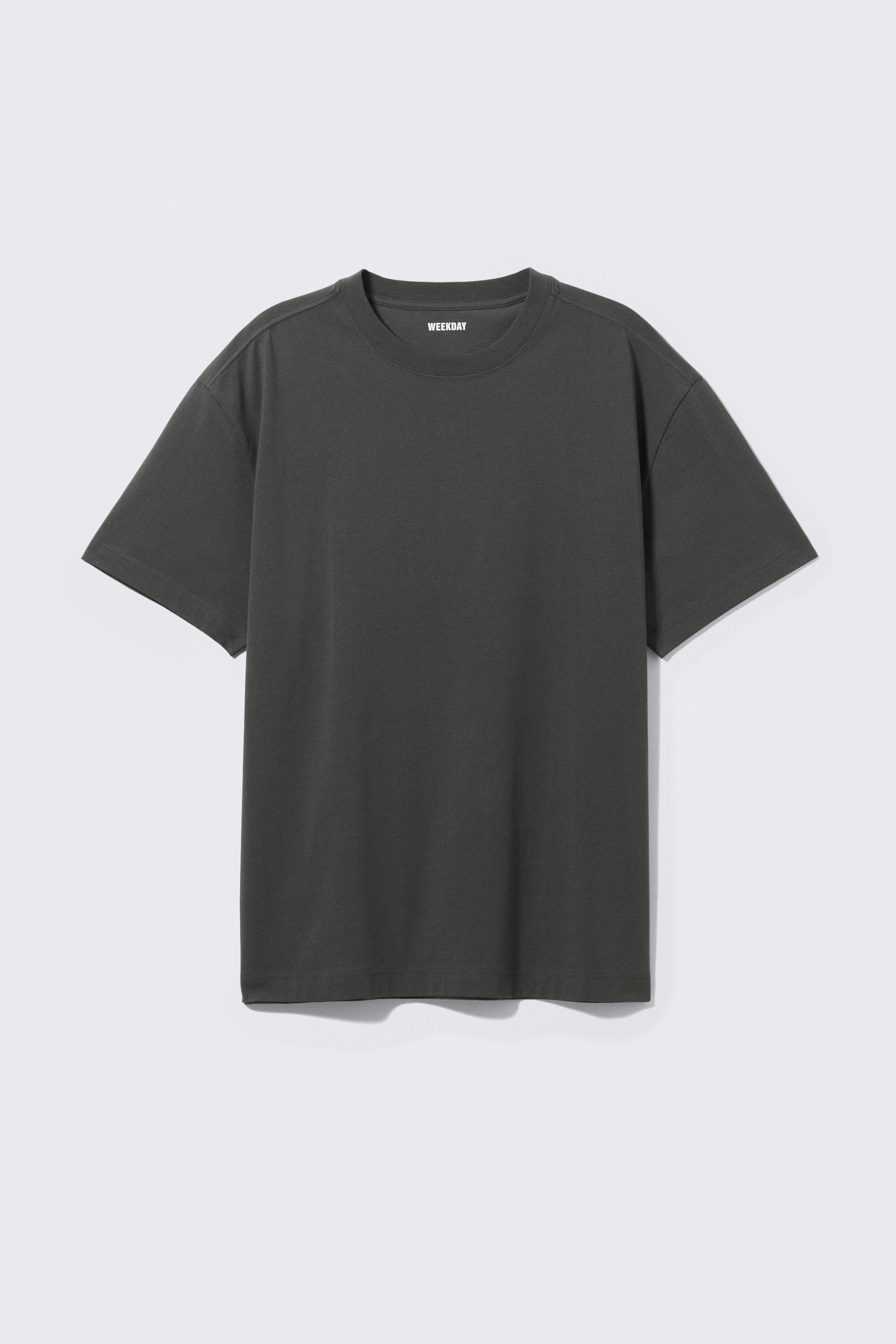 Grösseres Bild ansehen: Ein dunkelgraues T-Shirt wird präsentiert, mit einer lockeren Passform, Rundhalsausschnitt und kurzen, weiten Ärmeln mit überschnittenen Schultern. Der "WEEKDAY"-Markenname ist auf seinem inneren Nackenlabel sichtbar.
