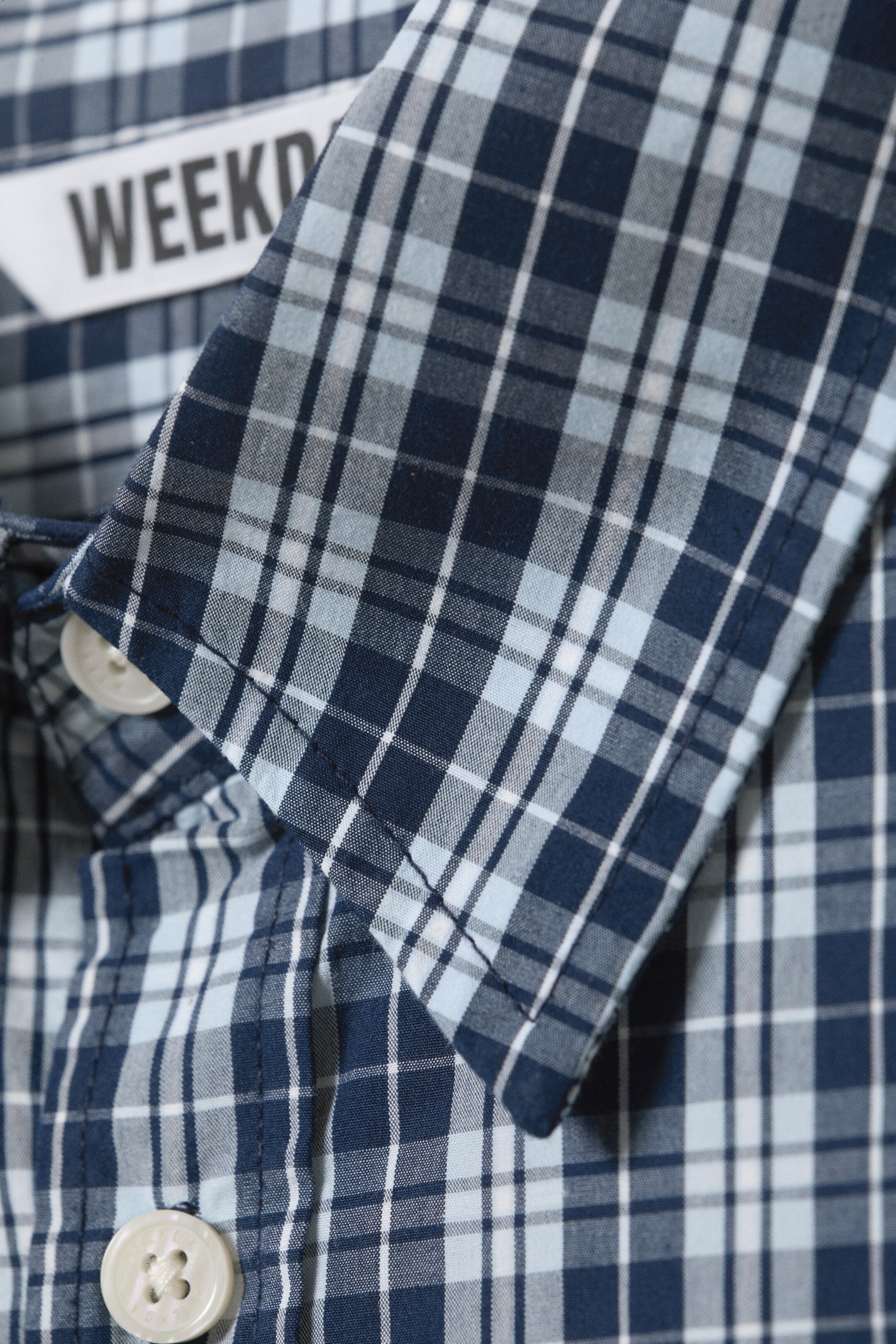 View larger image: A blue and white checked shirt is displaying a pointed collar, white buttons, and a visible 'WEEKDAY' brand tag on its inner collar.