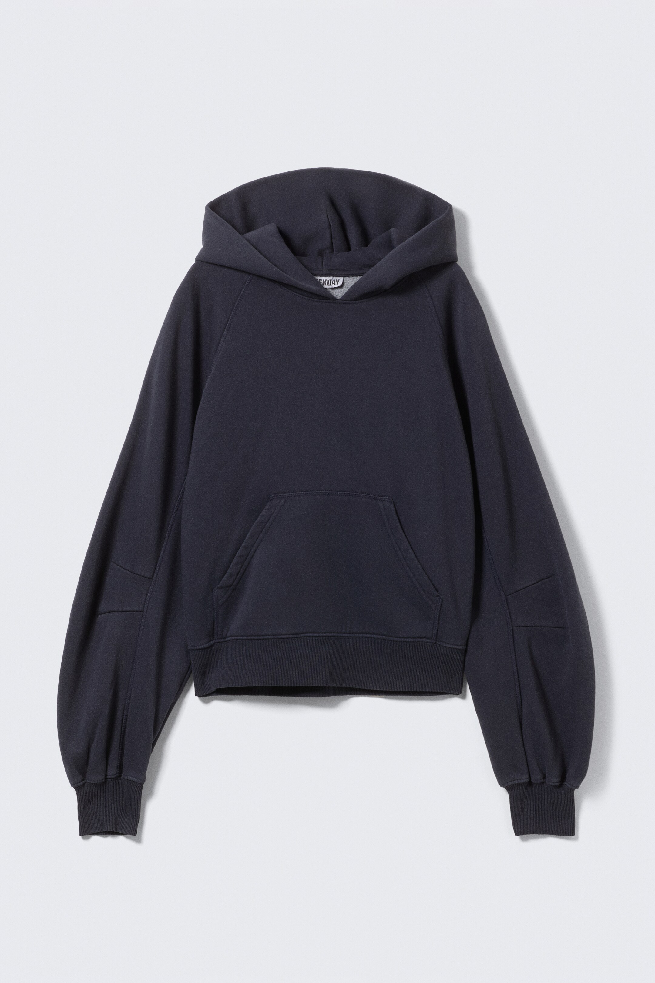 Größeres Bild ansehen: Ein dunkelgraues Hoodie wird von vorne gezeigt, mit einer kastigen Silhouette, Raglanärmeln und Paneeldetails an den äußeren Armen. Es ist mit einer geräumigen Kapuze mit abgenähten Details, einer Kängurutasche und breiten gerippten Abschlüssen an den Bündchen und am Saum gestaltet.