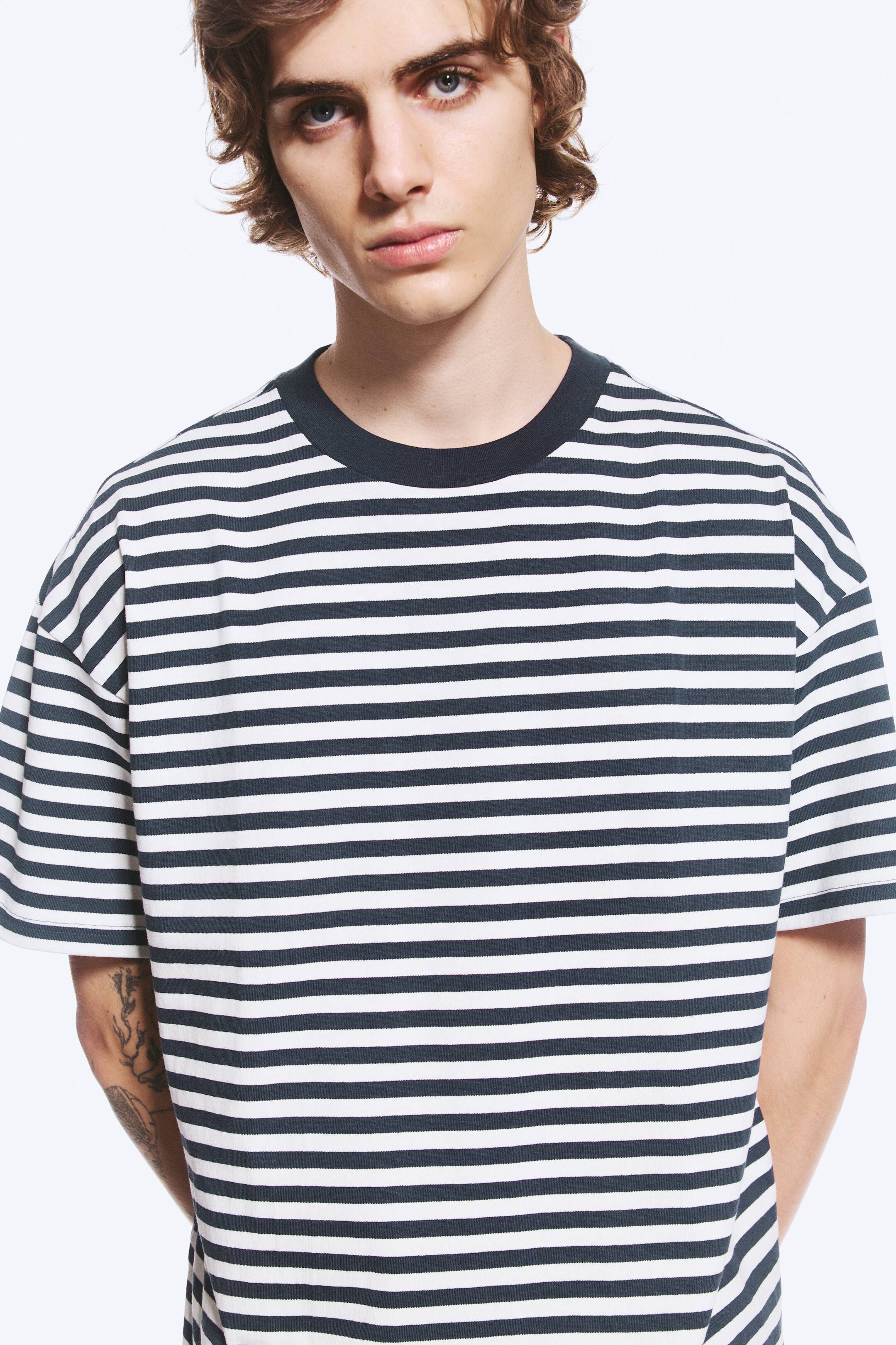 Προβολή μεγαλύτερης εικόνας: Ένα ριγέ T-shirt με οριζόντιες ρίγες σε σκούρο ναυτικό μπλε και υπόλευκο φοριέται από το μοντέλο. Το T-shirt διαθέτει μονόχρωμη σκούρα ναυτική μπλε στρογγυλή λαιμόκοψη, χαμηλωμένους ώμους και άνετη εφαρμογή.