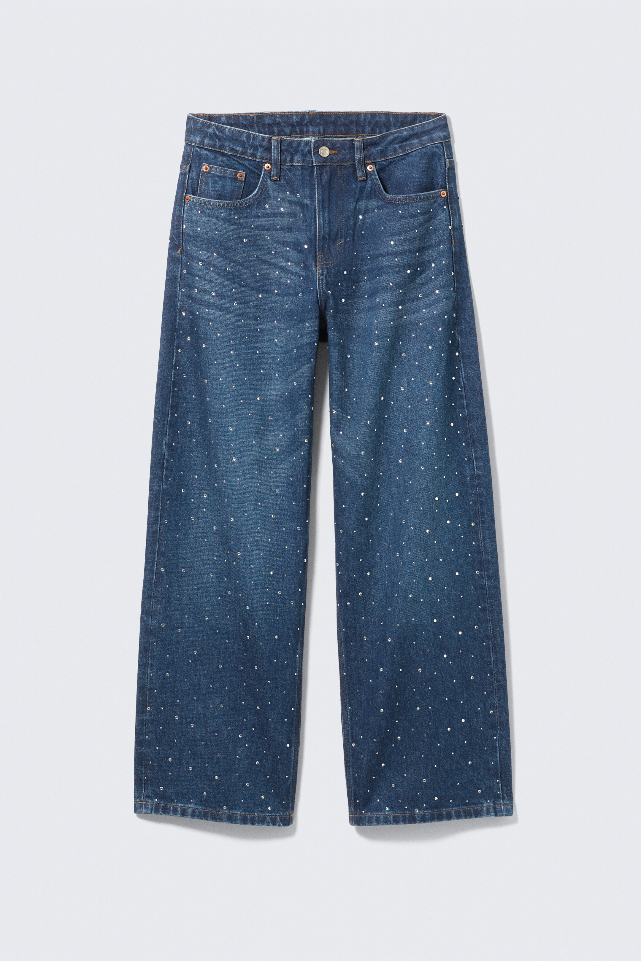Visualizza immagine più grande: Jeans in denim blu scuro sono mostrati dalla PARTE ANTERIORE, caratterizzati da borchie sparse tono argento su tutta la superficie anteriore. Sono progettati con un taglio a gamba larga, chiusura con bottone e zip, passanti per cintura e uno stile a cinque tasche, con cuciture a contrasto che delineano le cuciture e le tasche.