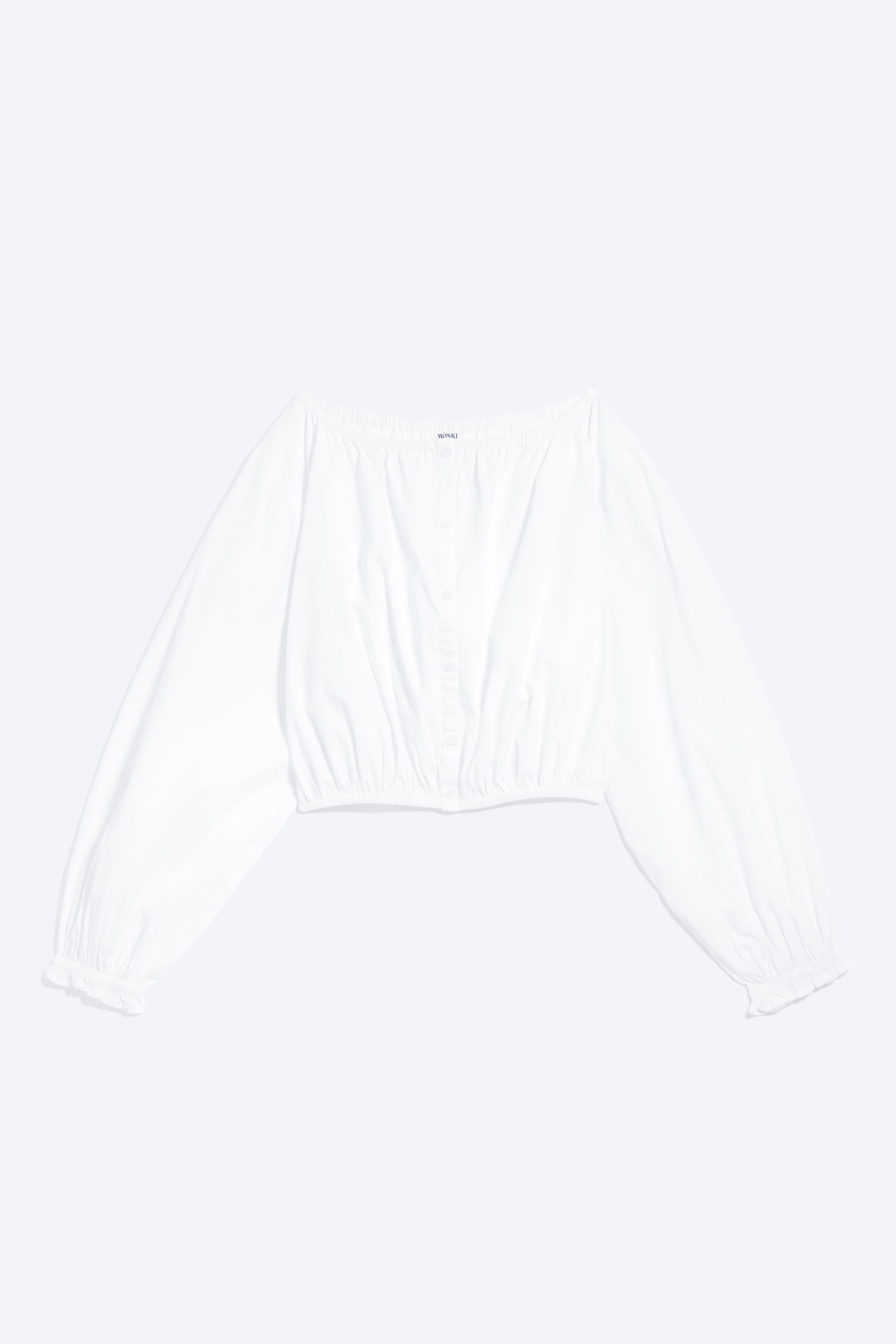 Visa större bild: En vit crop top visas i frontvy, med en elastisk halsringning och knäppning framtill. Den har långa, voluminösa ärmar med elastiska muddar och en elastisk nederkant.
